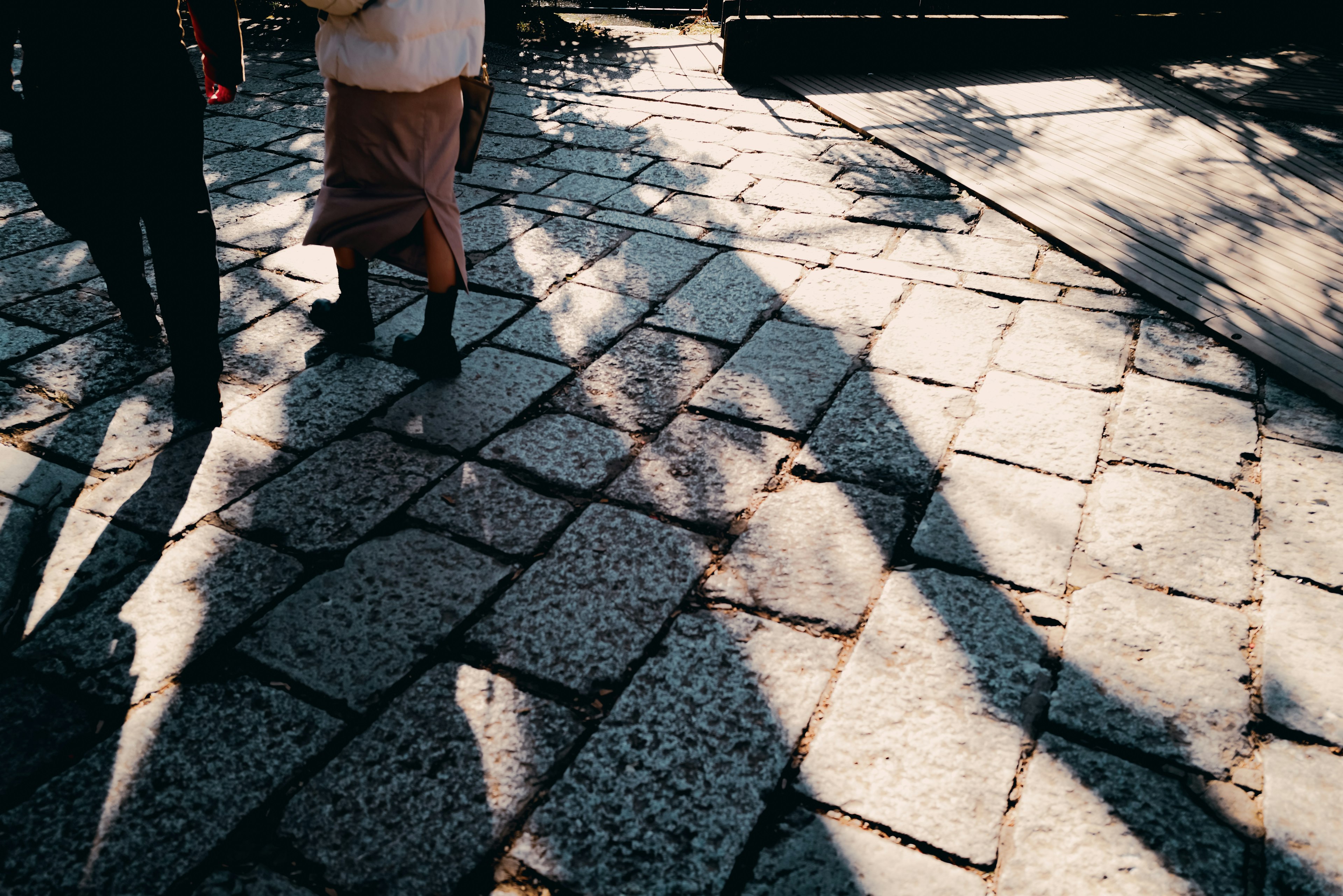 Personas caminando sobre un pavimento de piedra con luces y sombras entrelazadas