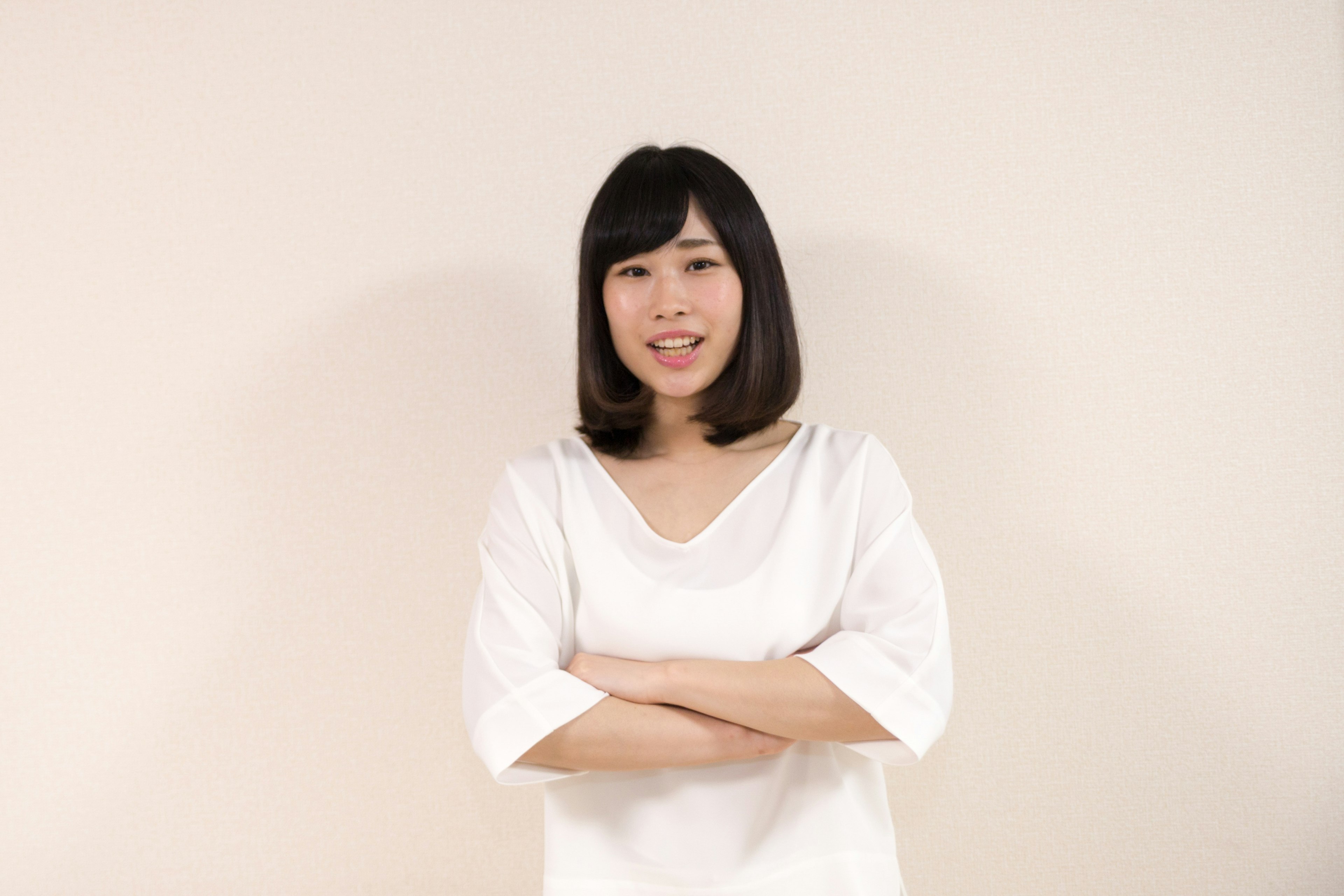 A woman in a white shirt standing with arms crossed and smiling