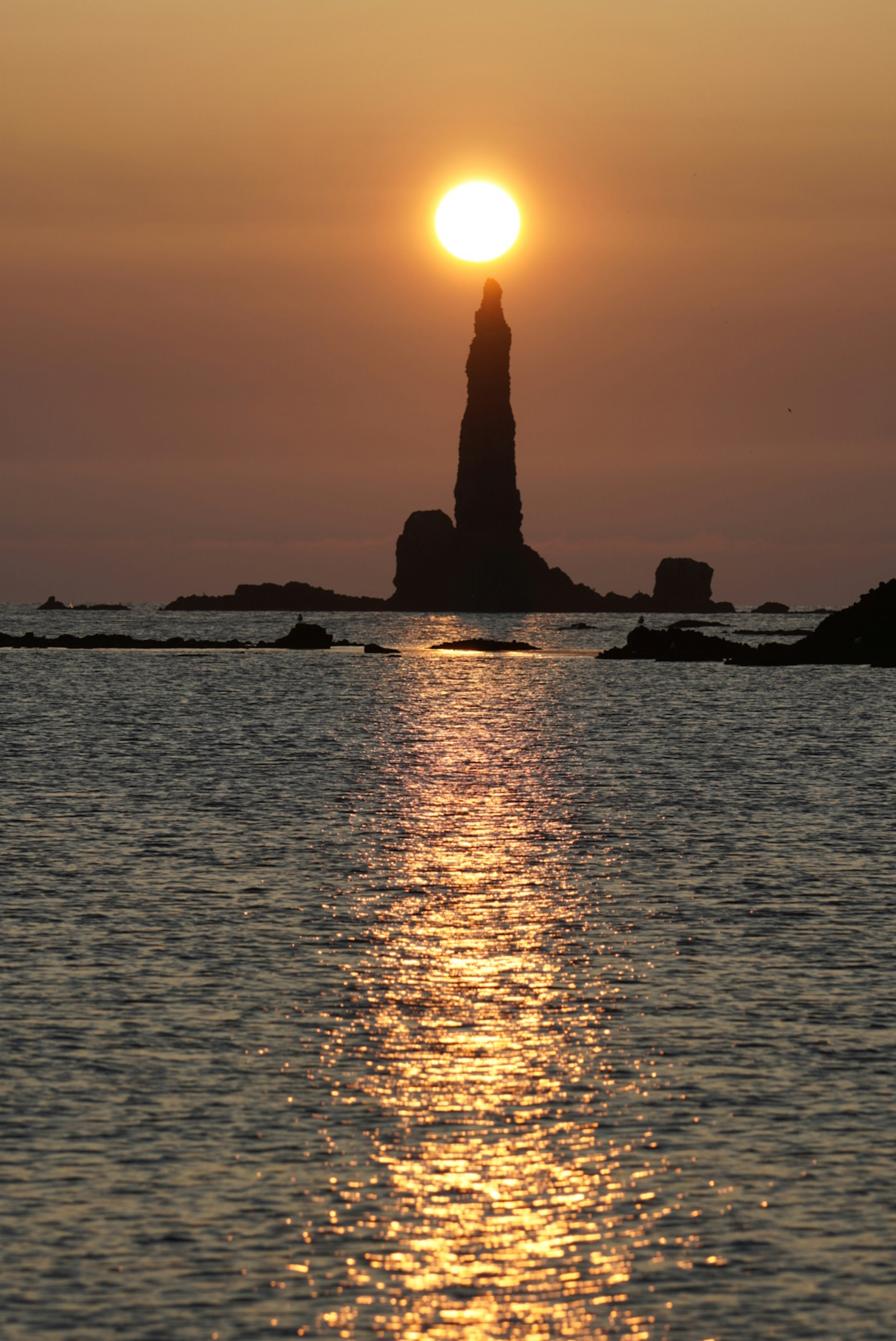 夕陽在海中的高岩石後面落下