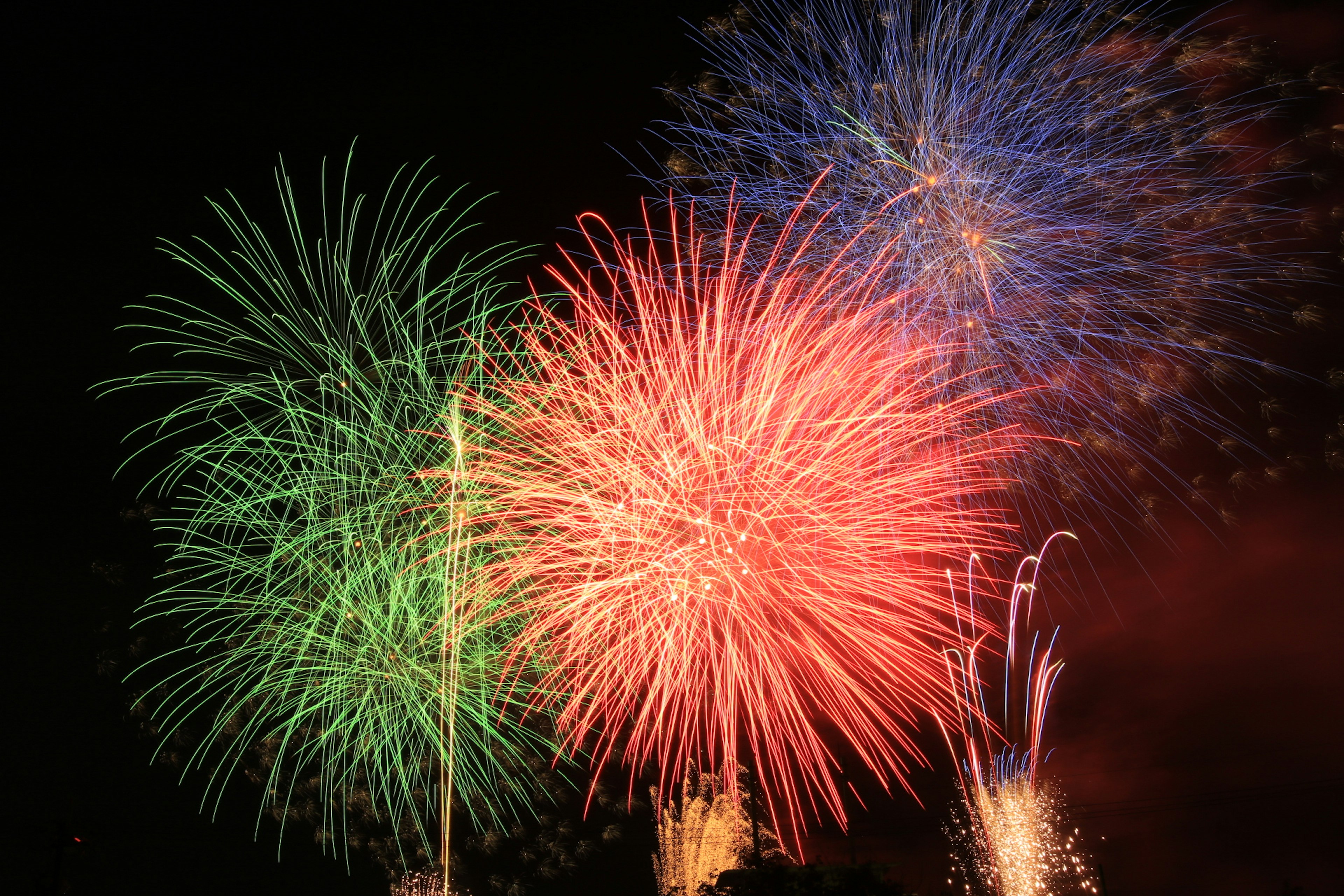 夜空に大きな花火が打ち上げられ青、緑、赤の色彩が広がる