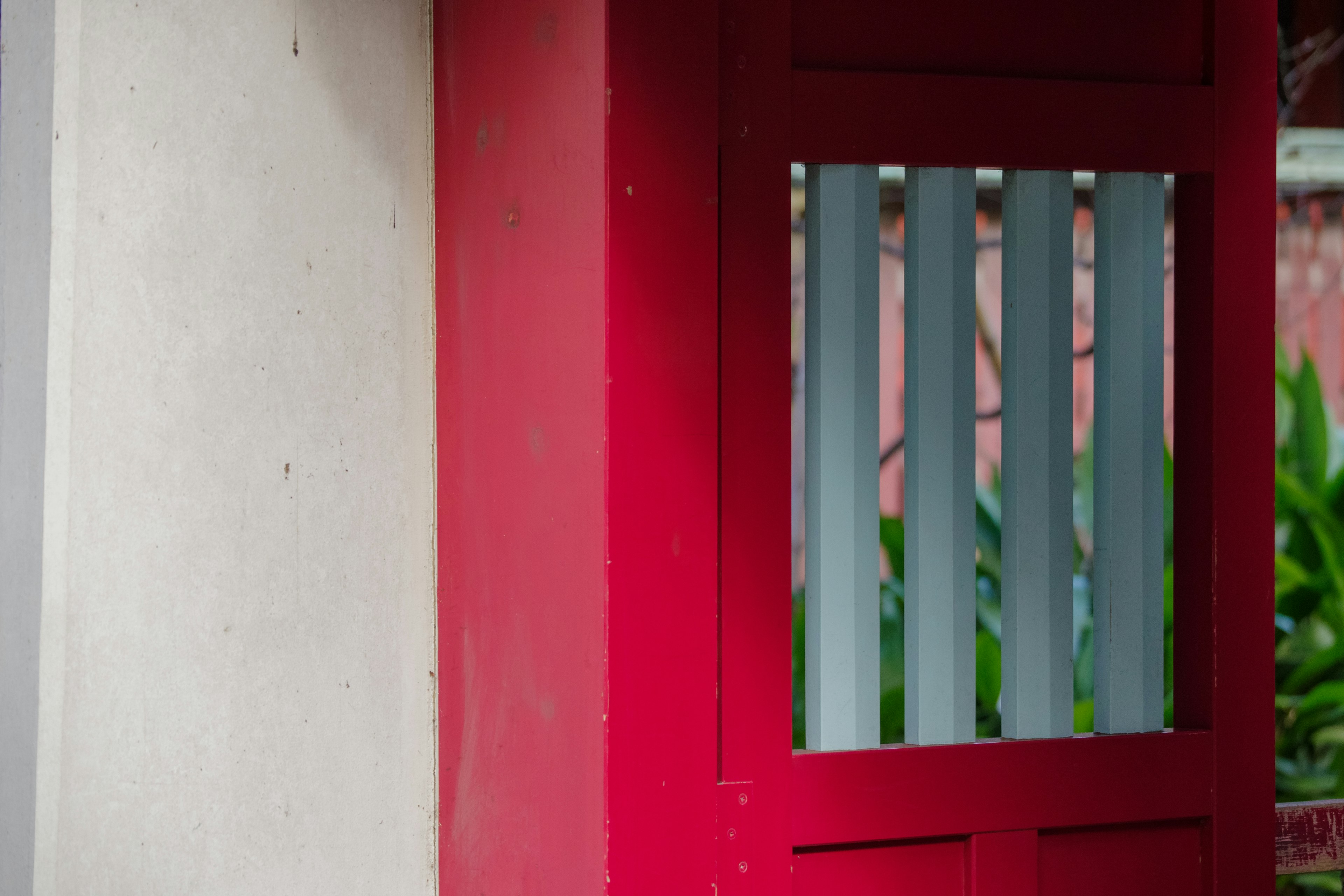 Gambar yang menampilkan pintu merah dengan slat vertikal dan dinding putih