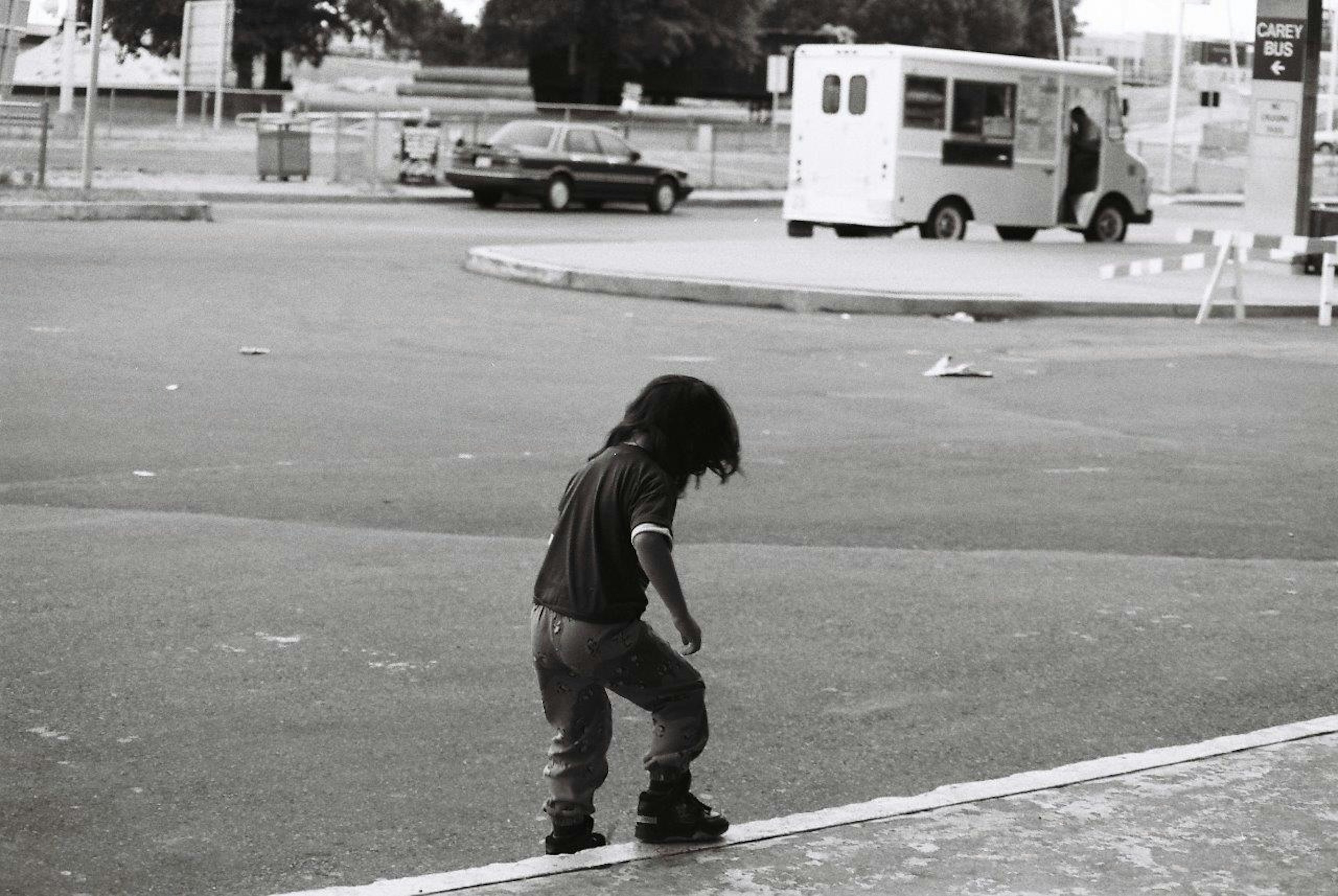 Foto en blanco y negro de un niño de pie al borde de una carretera con coches y un vehículo postal al fondo