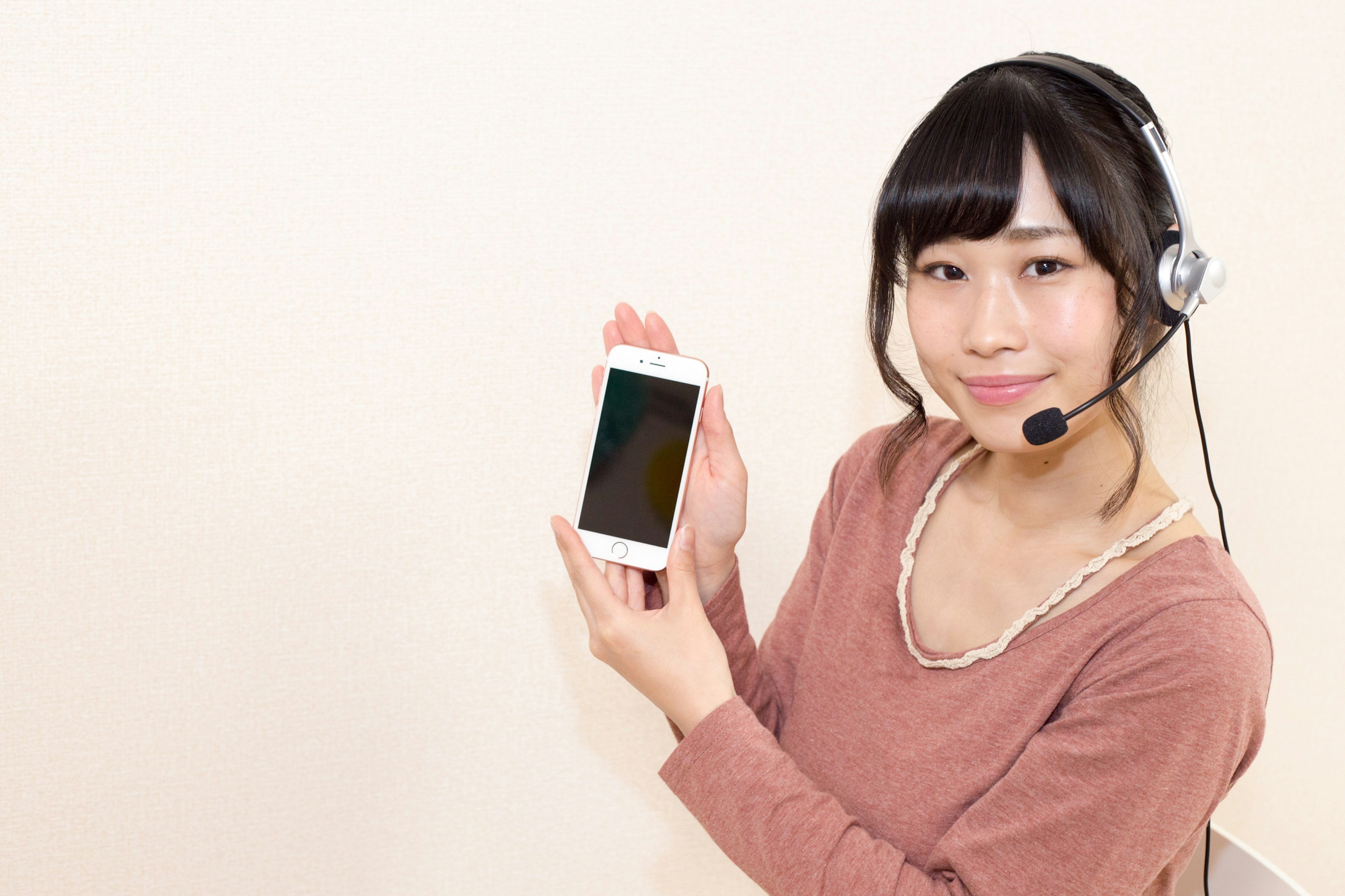 A woman wearing a headset holding a smartphone and smiling