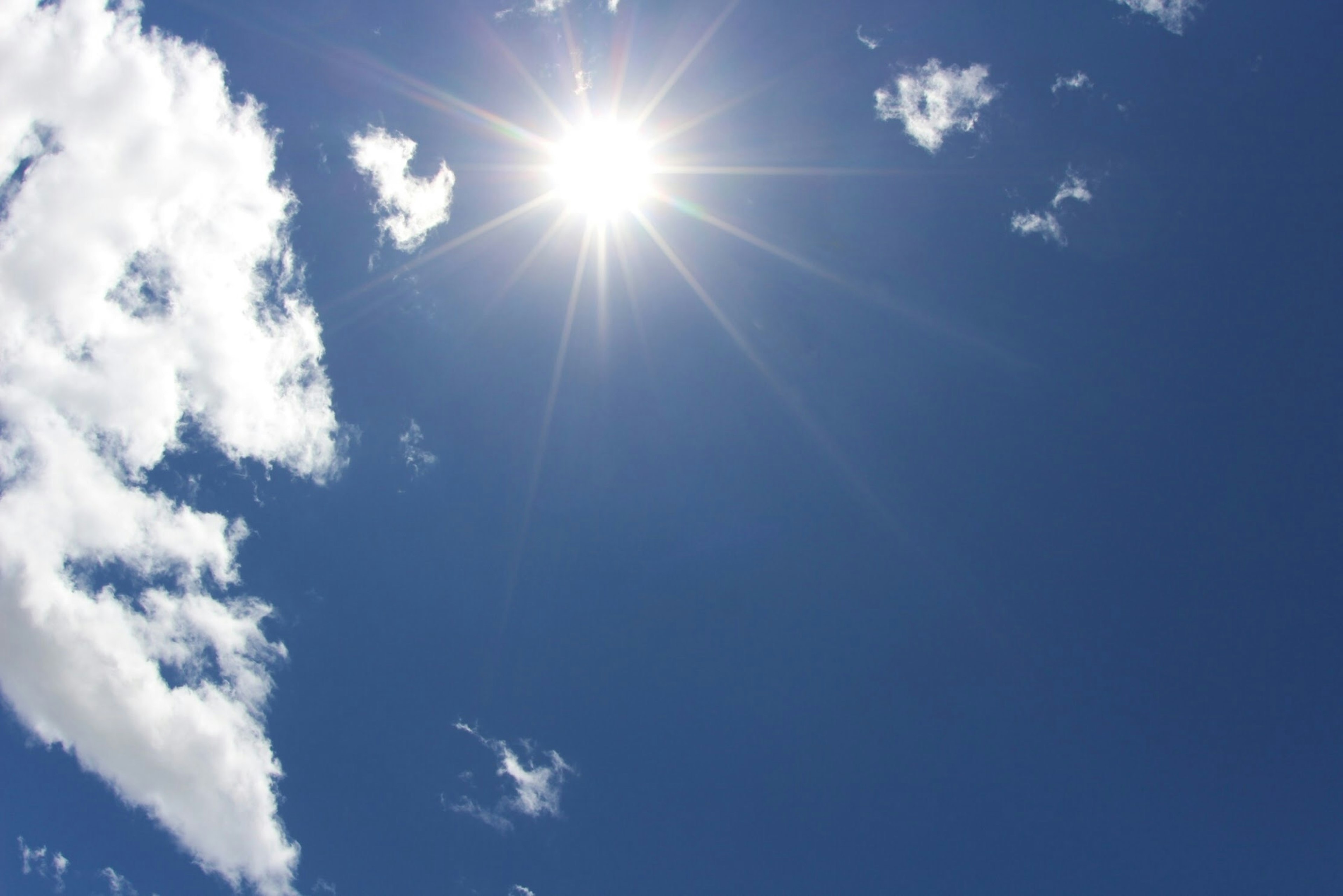 Bright sun shining in a clear blue sky with white clouds