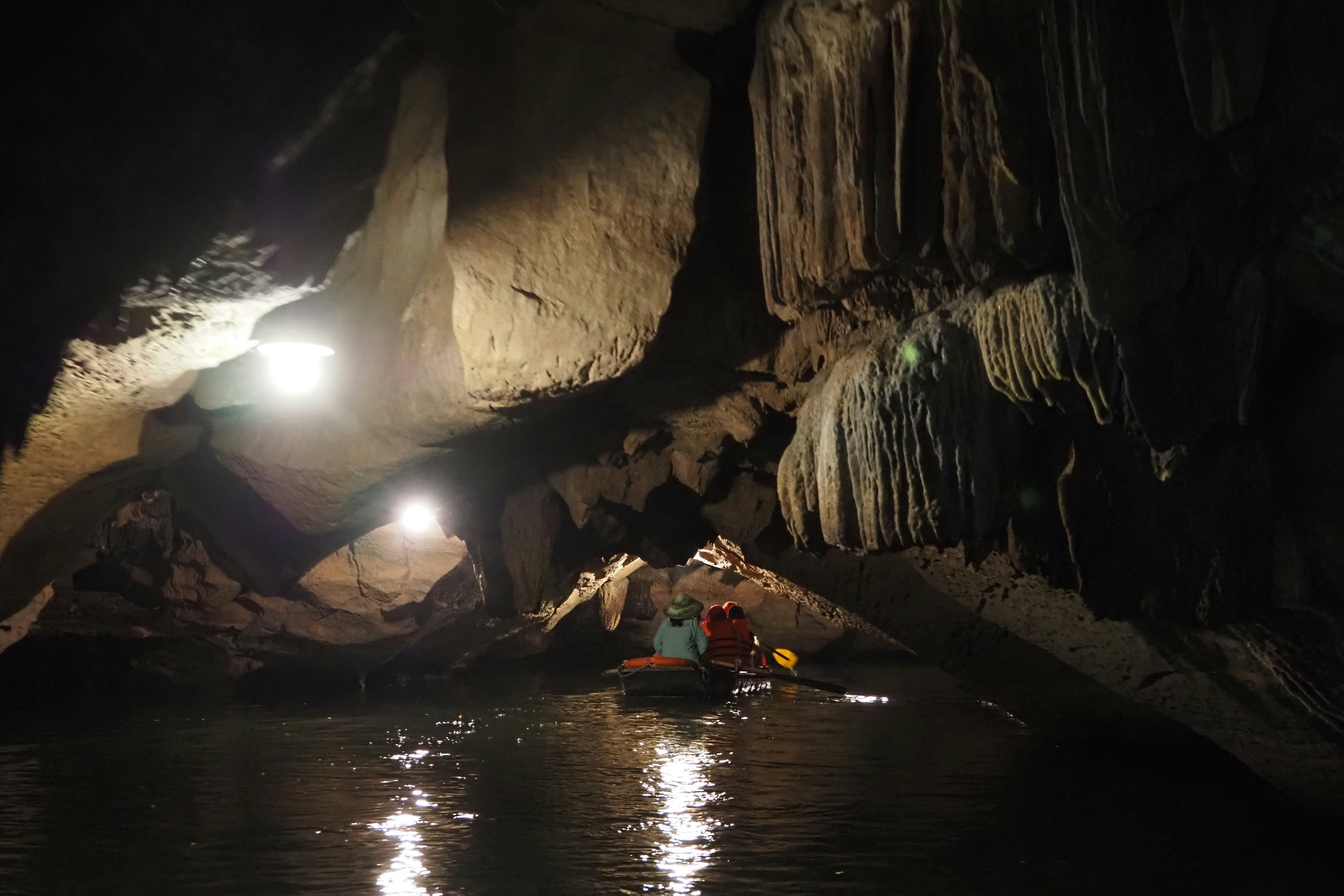 People kayaking in a dark cave with lights reflecting on the water