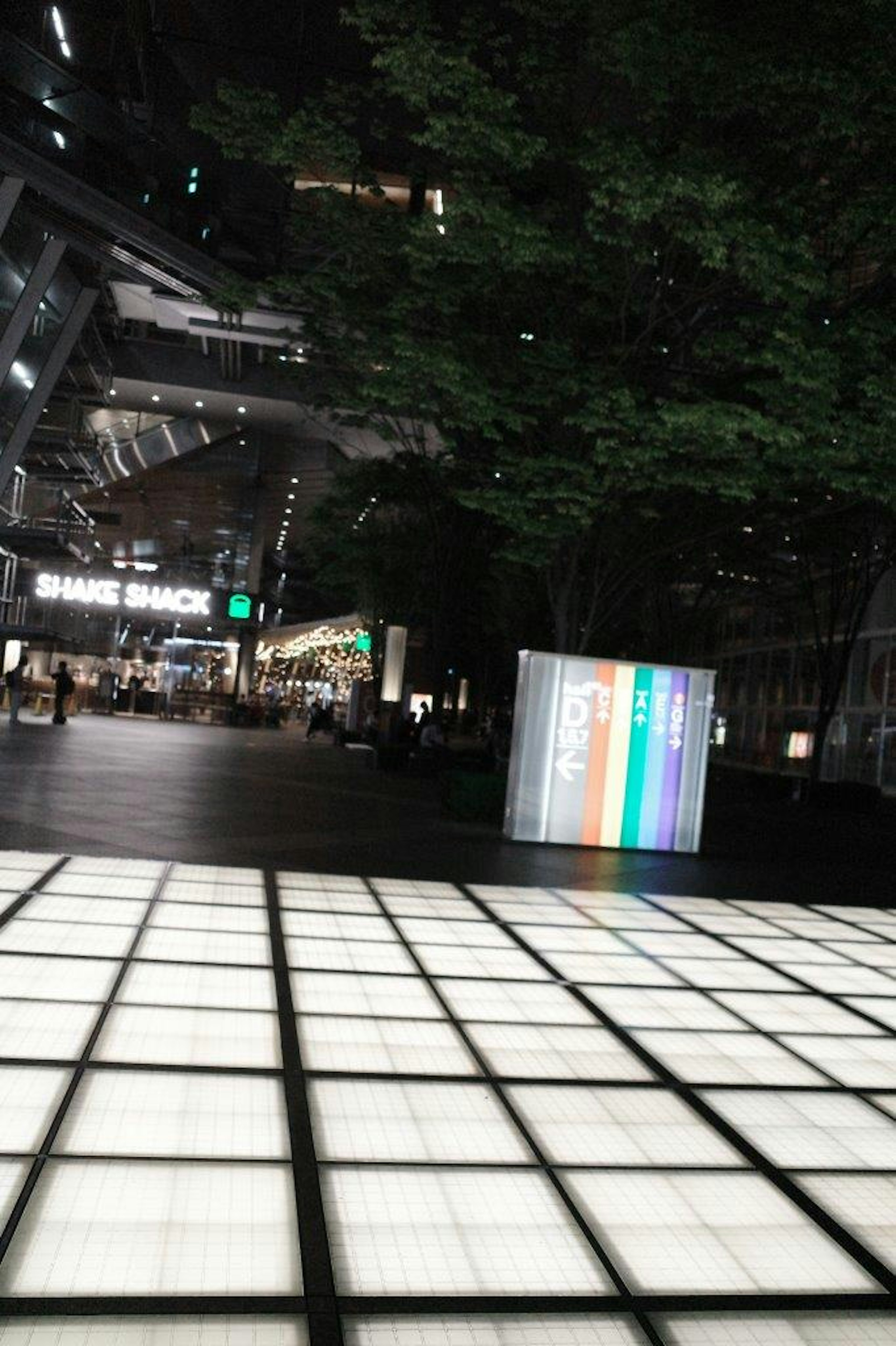 Illuminated tiles in a nighttime urban space with a colorful box