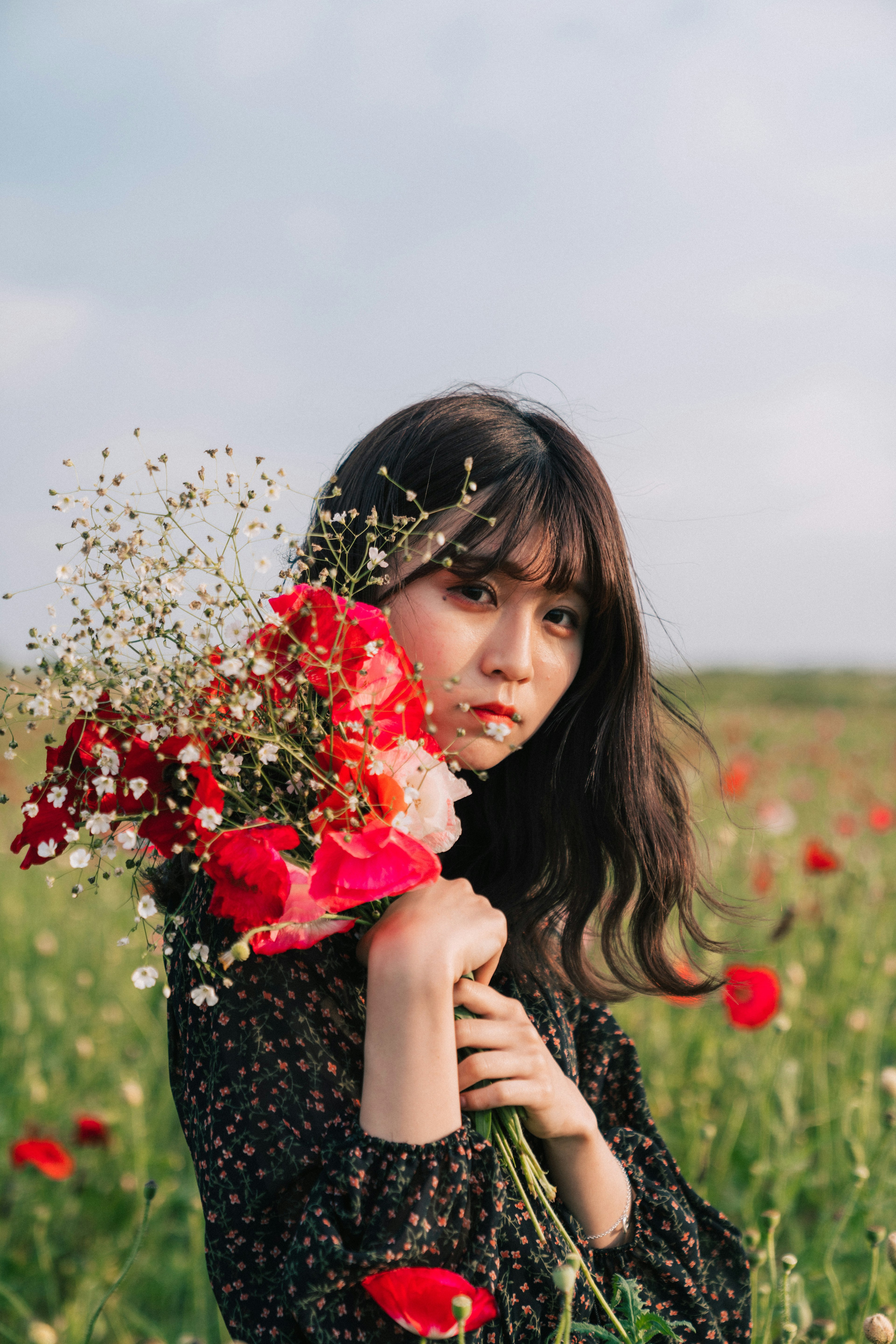 野花の中で赤い花束を持つ女性のポートレート