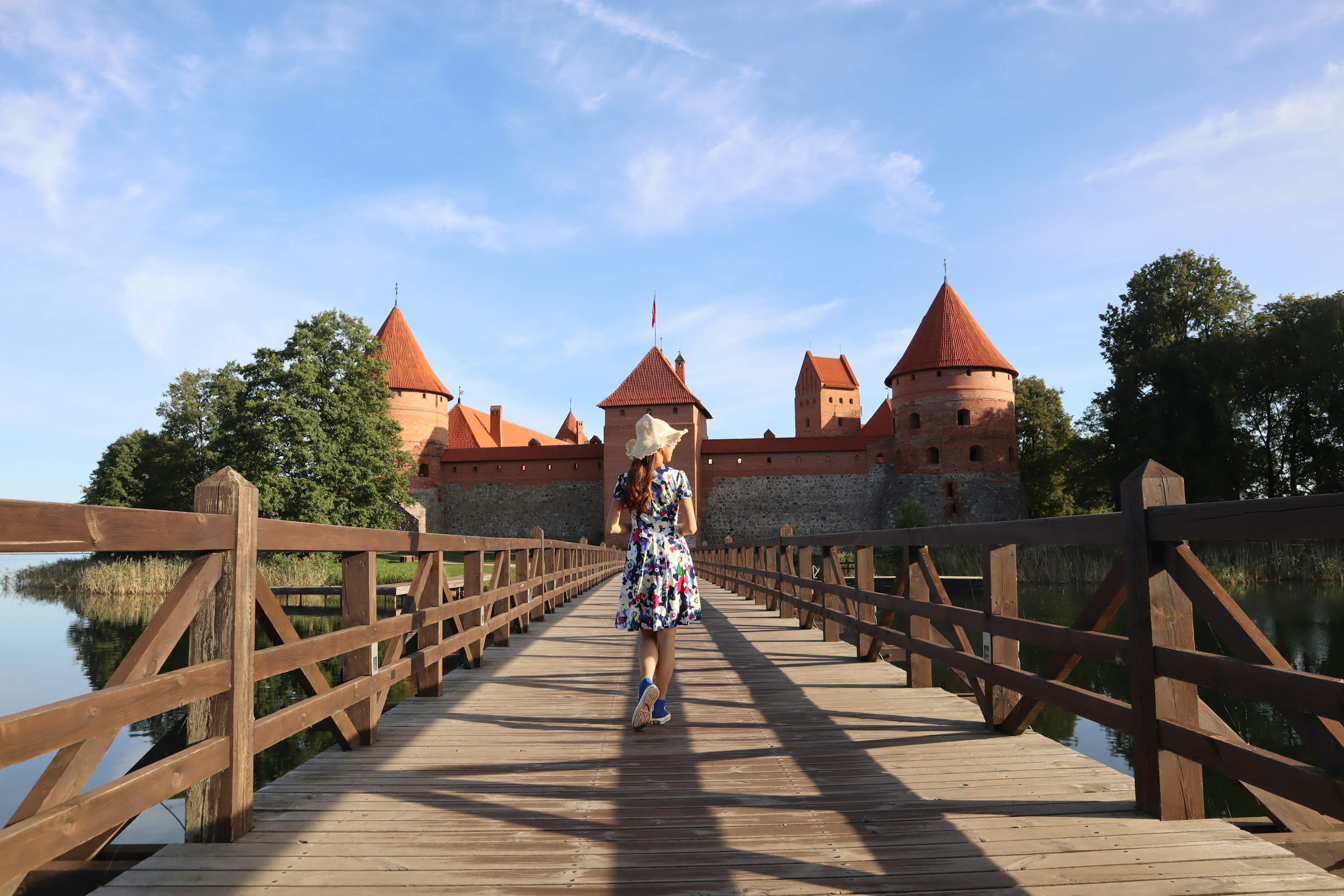 Femme marchant sur un pont en bois vers le château de Trakai avec des toits rouges