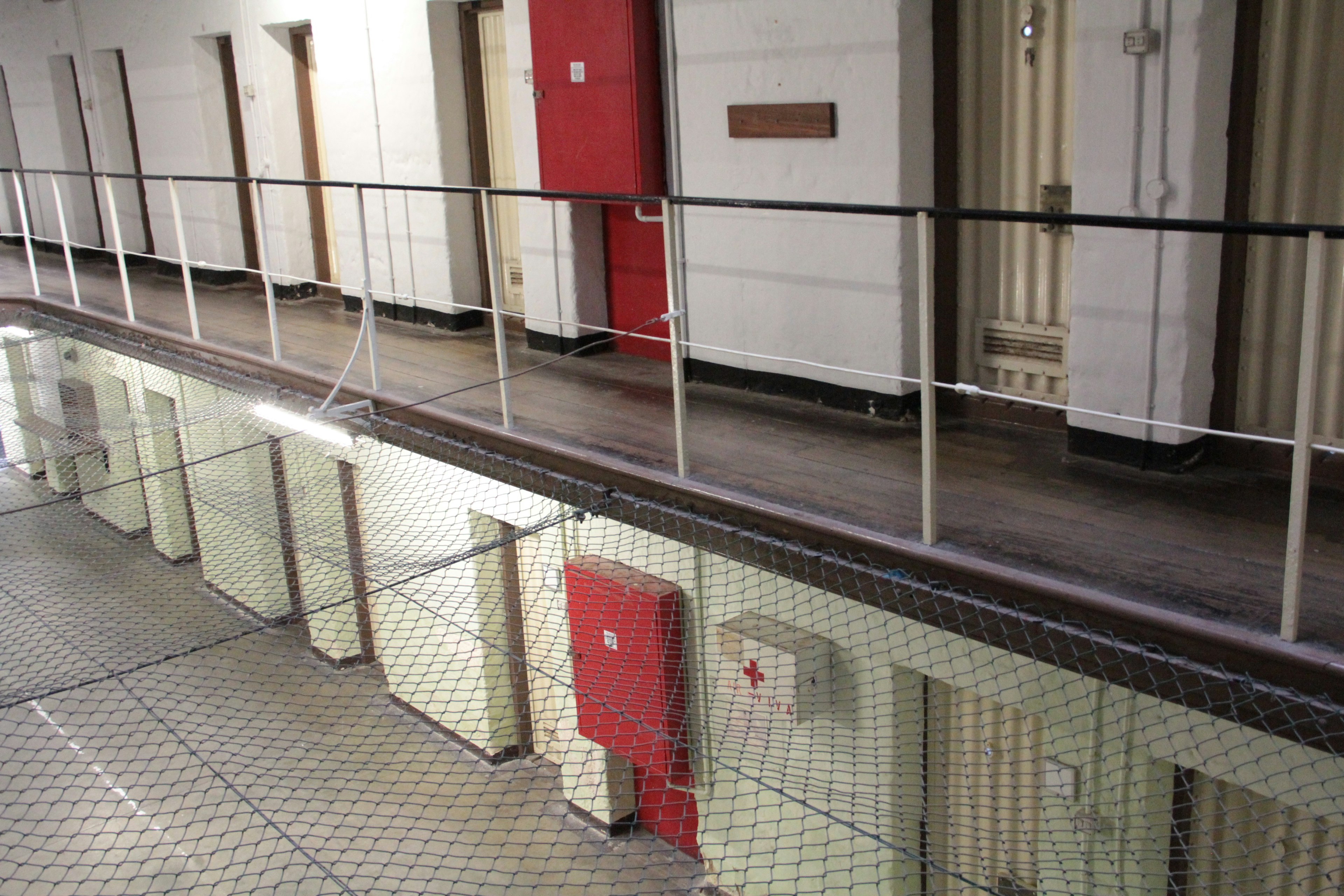 View of a prison corridor with red doors and white walls