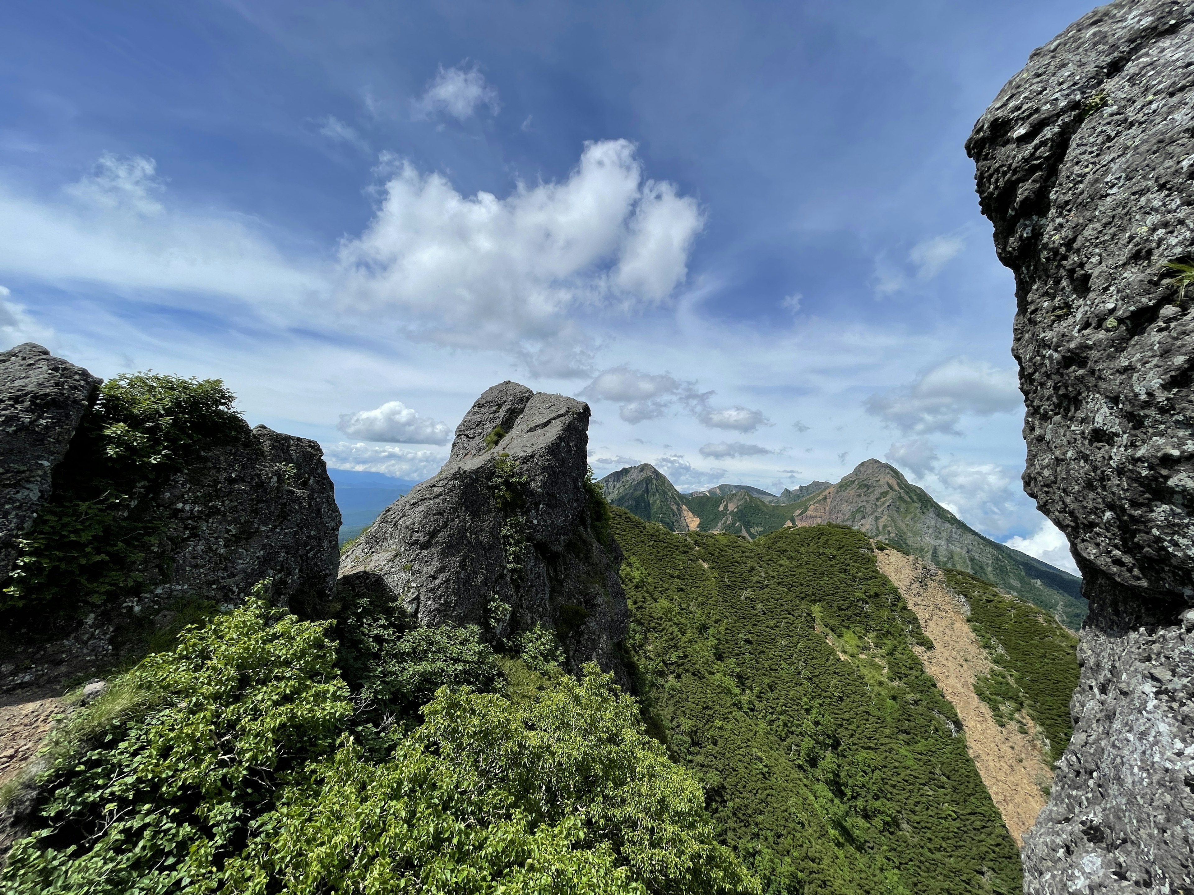 Panoramablick von einem Berggipfel üppige grüne Hügel und blauer Himmel markante große Felsen