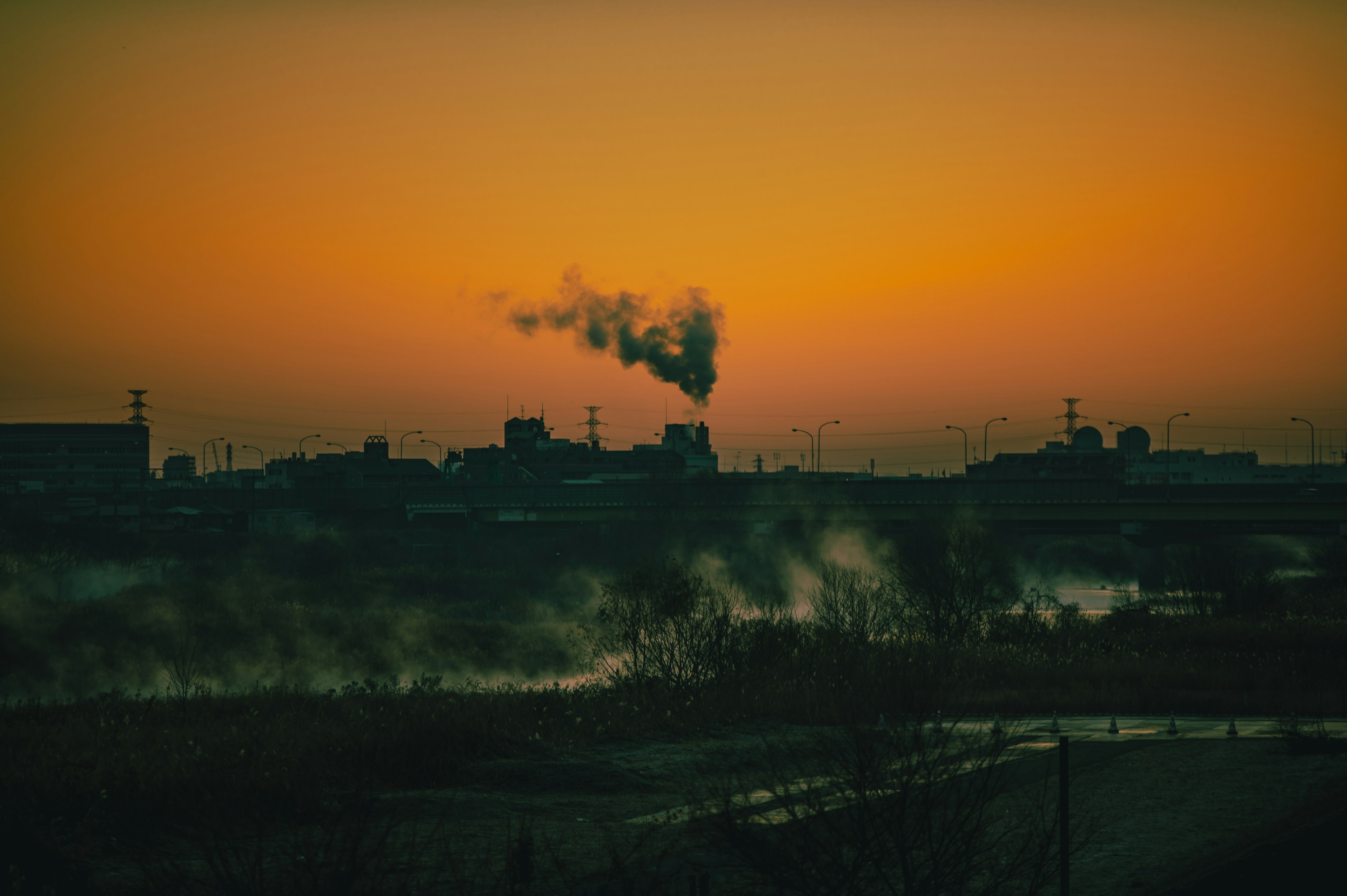 Silueta de una fábrica emitiendo humo contra un cielo al atardecer