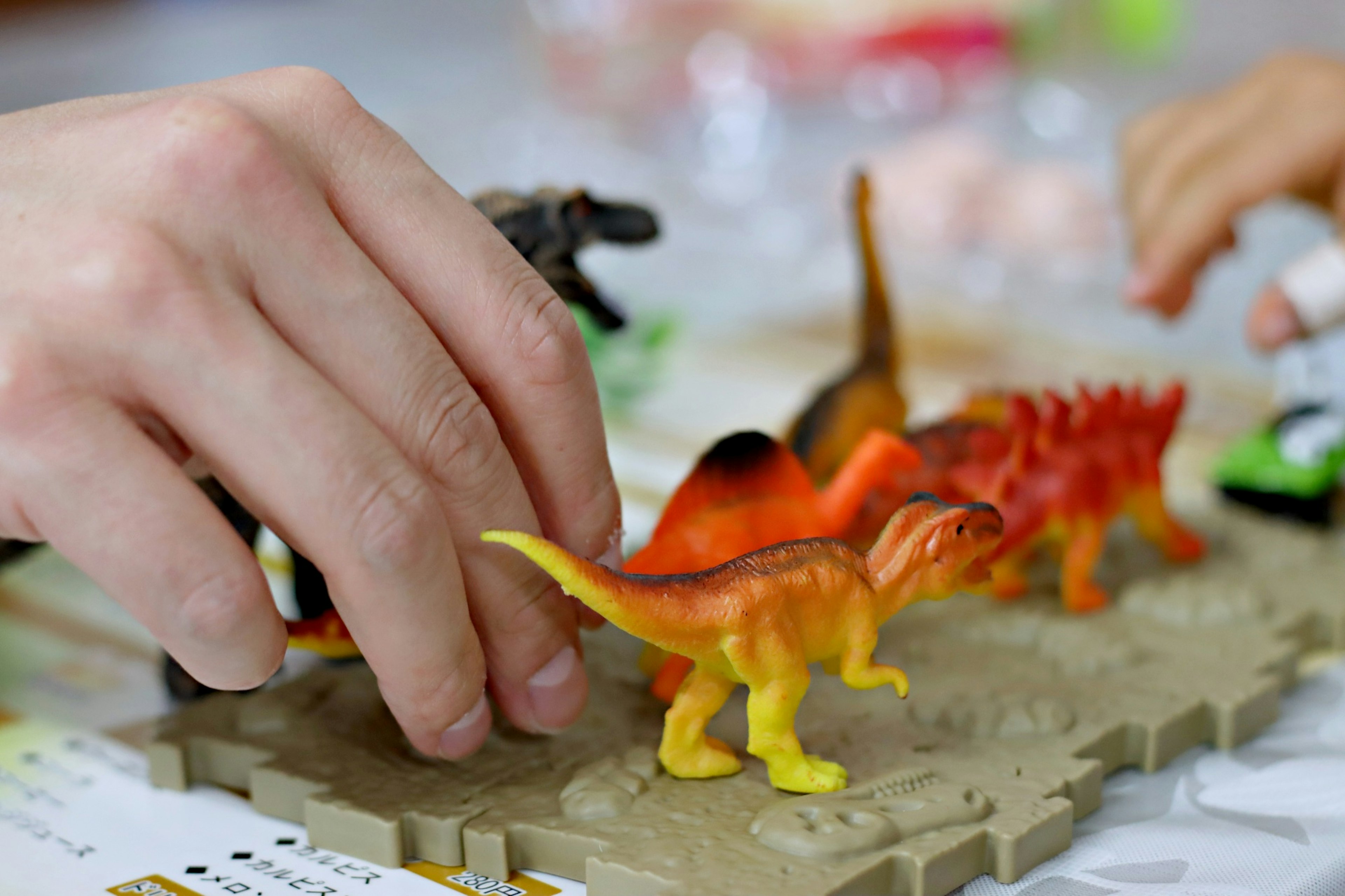 A hand manipulating colorful dinosaur toys on a play mat