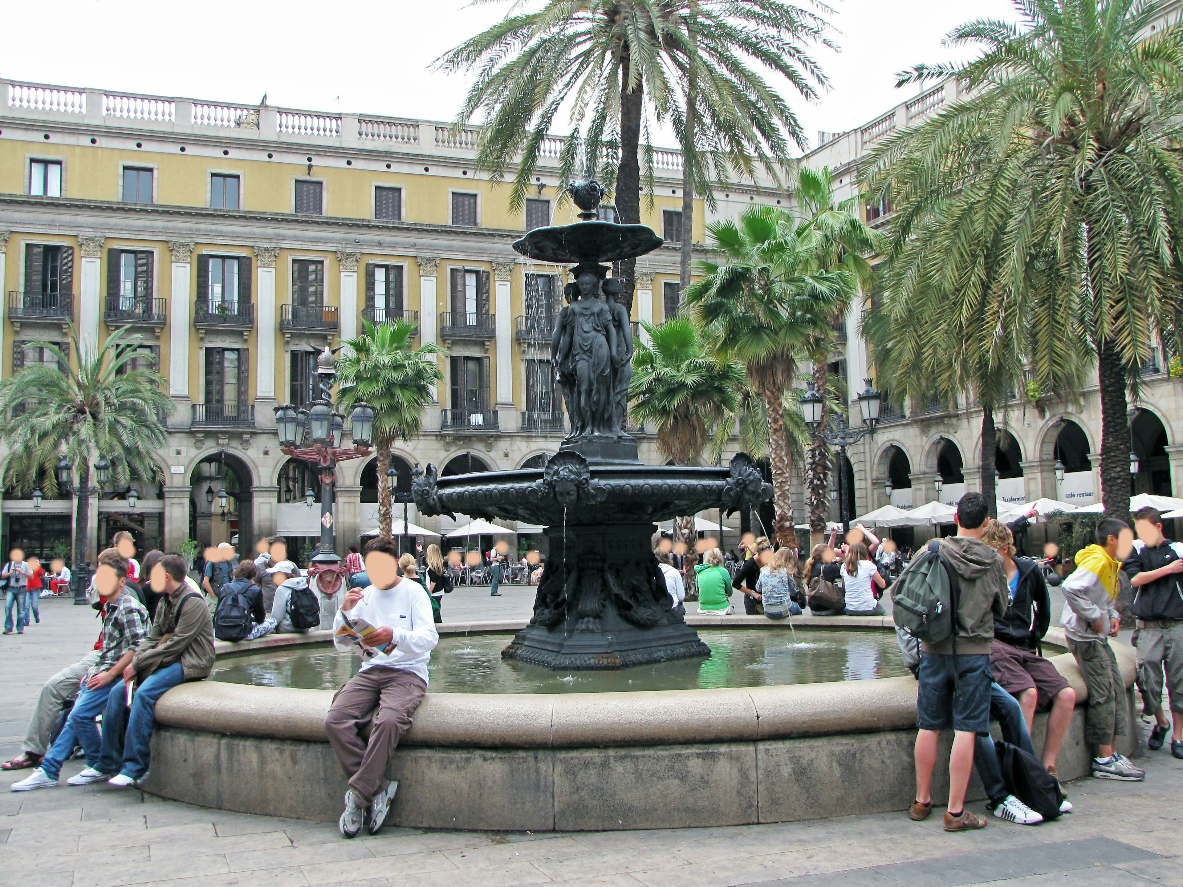 Fountain in a Barcelona square surrounded by palm trees and people sitting