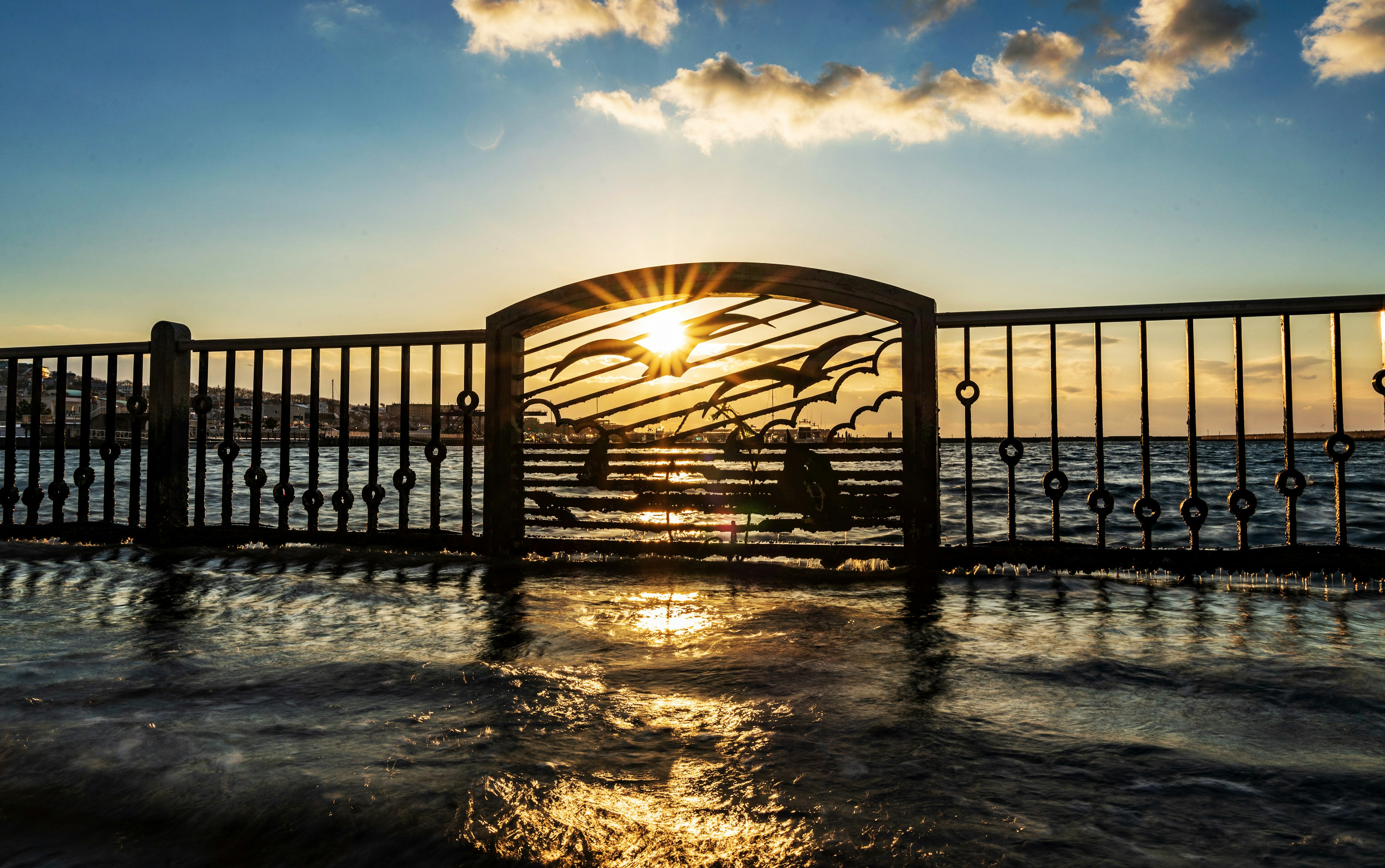 海辺の鉄のフェンス越しに見える夕日と水面の反射