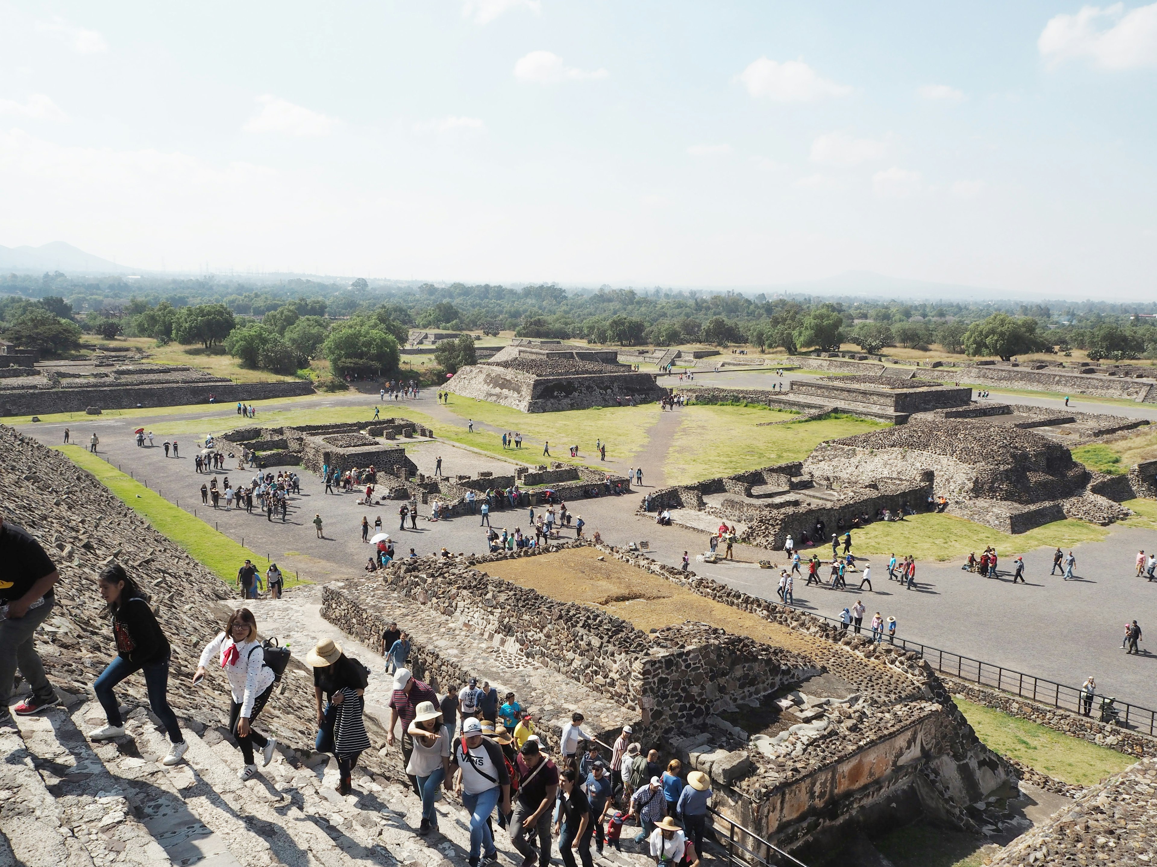 Besucher steigen Treppen in Teotihuacan mit Pyramiden im Hintergrund