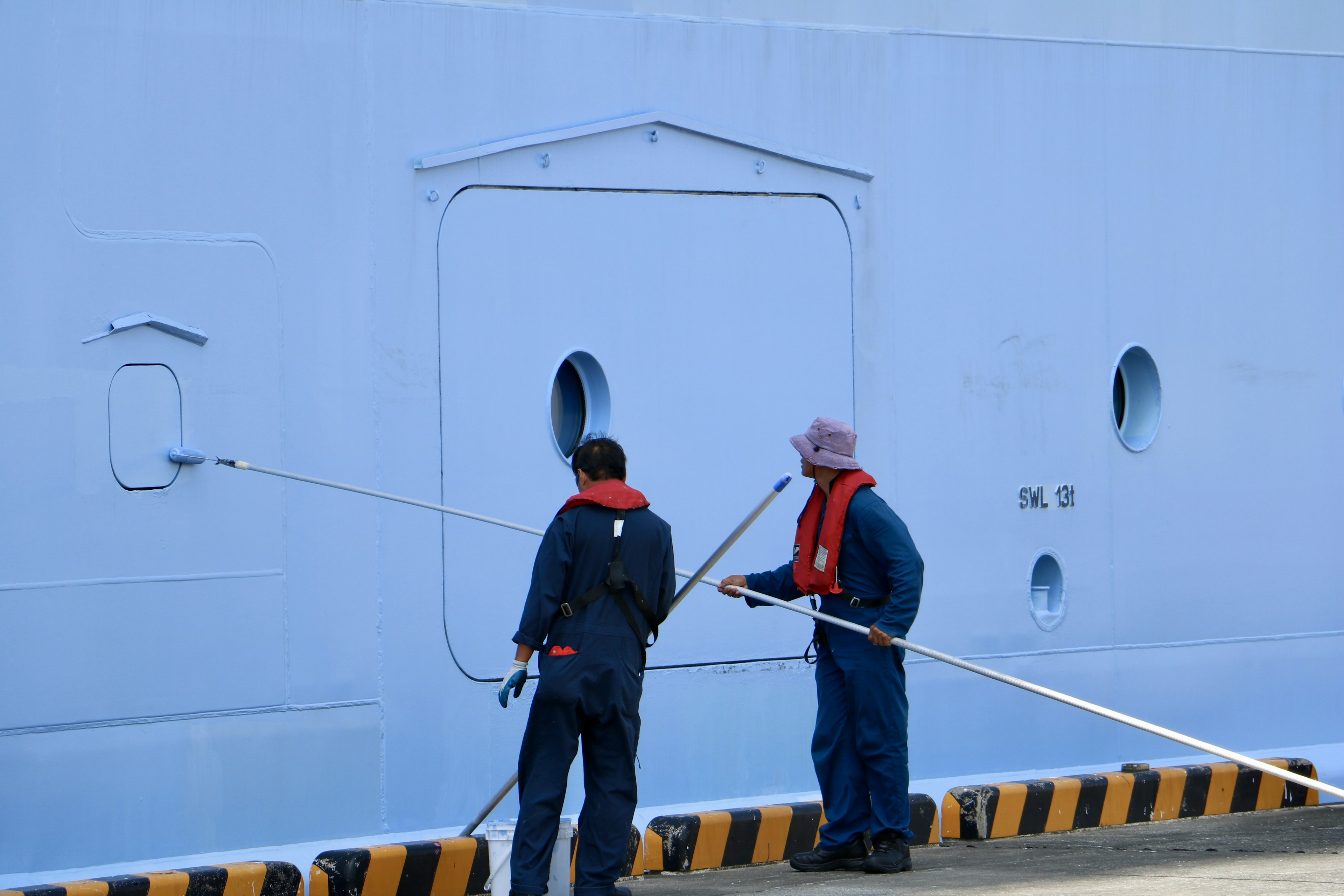 Dos trabajadores en el costado de un barco con casco azul y aberturas