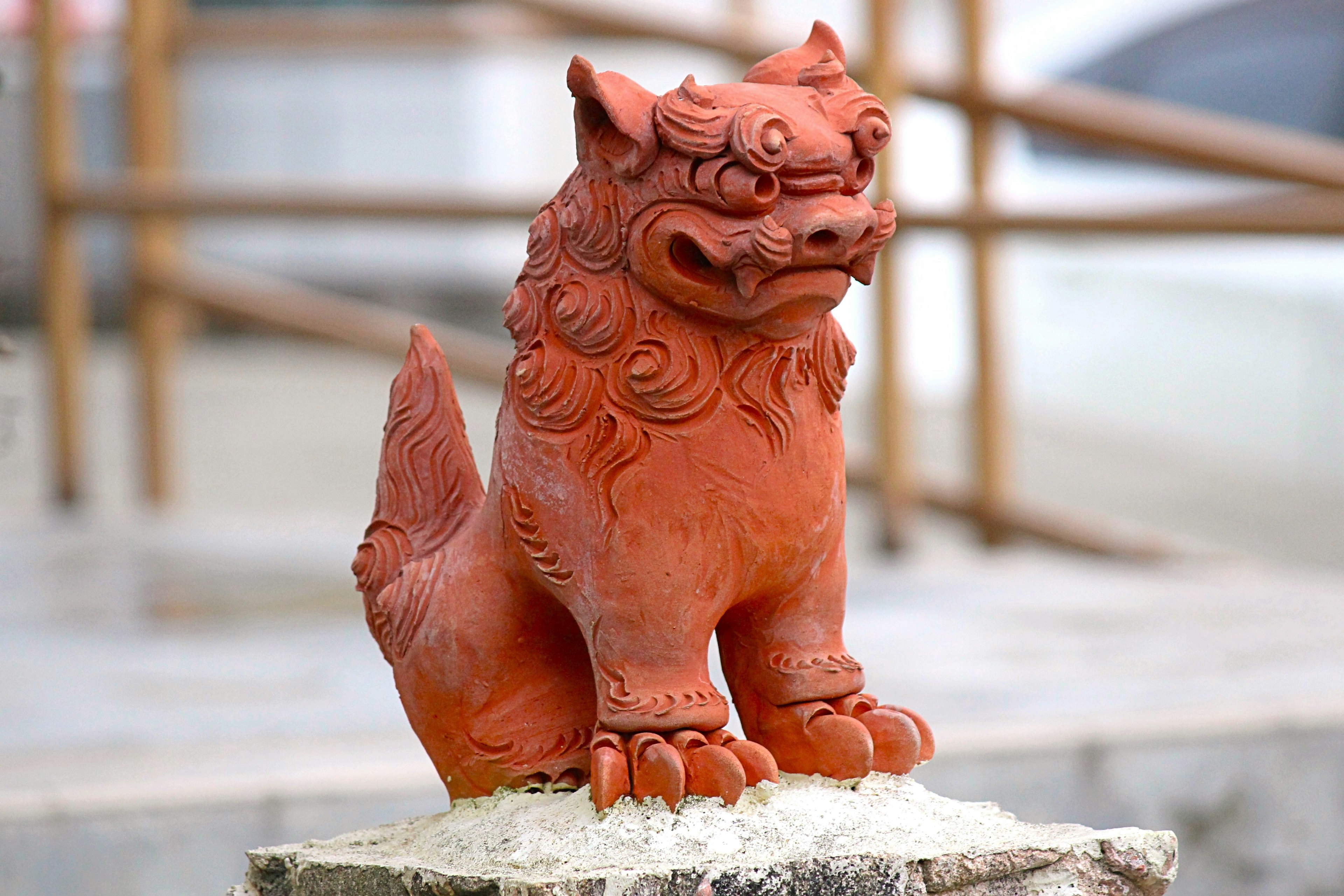 A clay statue of a lion-dog sitting on a pedestal