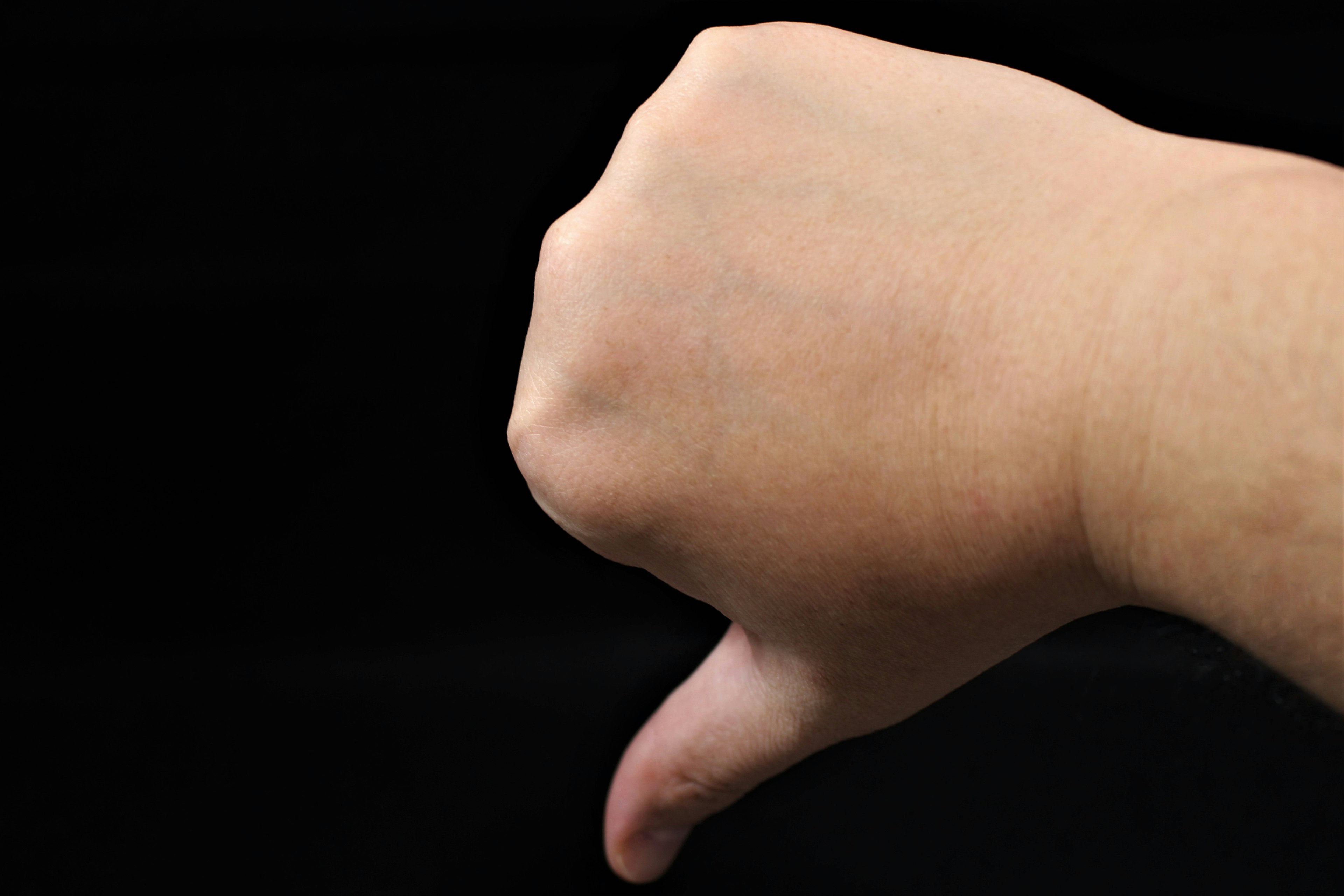 Hand making a thumbs down gesture against a black background