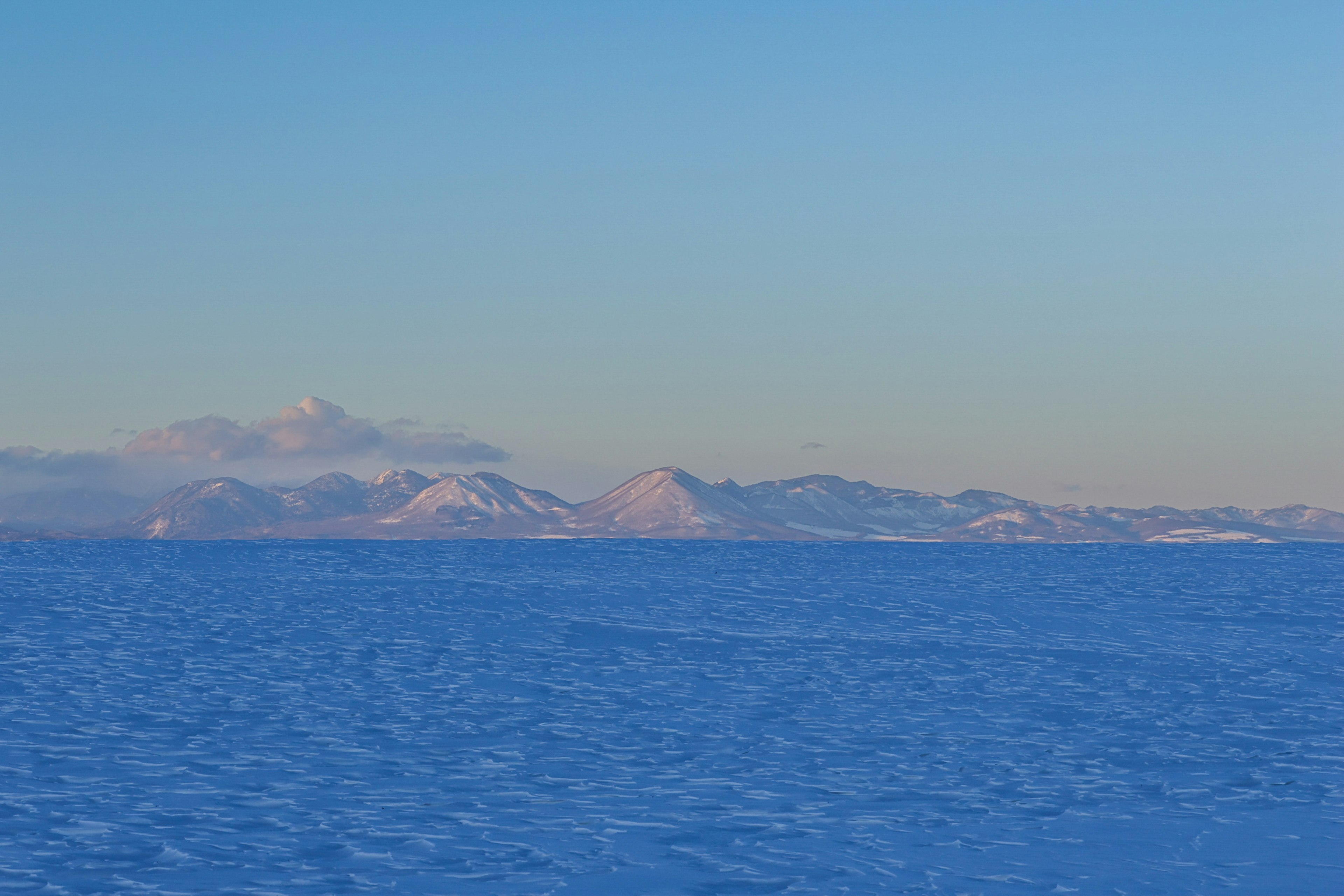 雪に覆われた山々が青い海の向こうに広がる風景