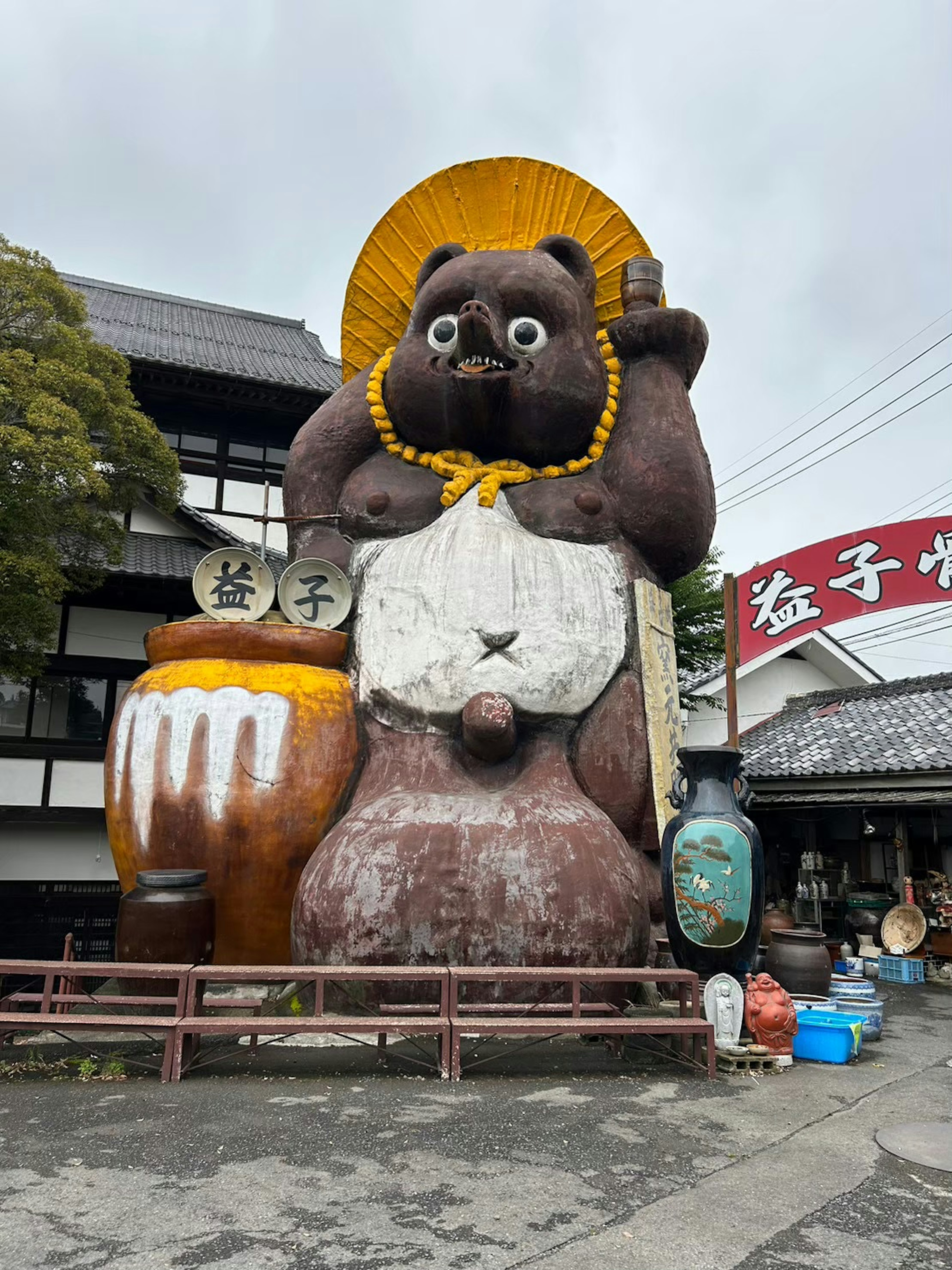 大きな狸の像が傘を持ち、周囲には陶器や木の桶が並ぶ