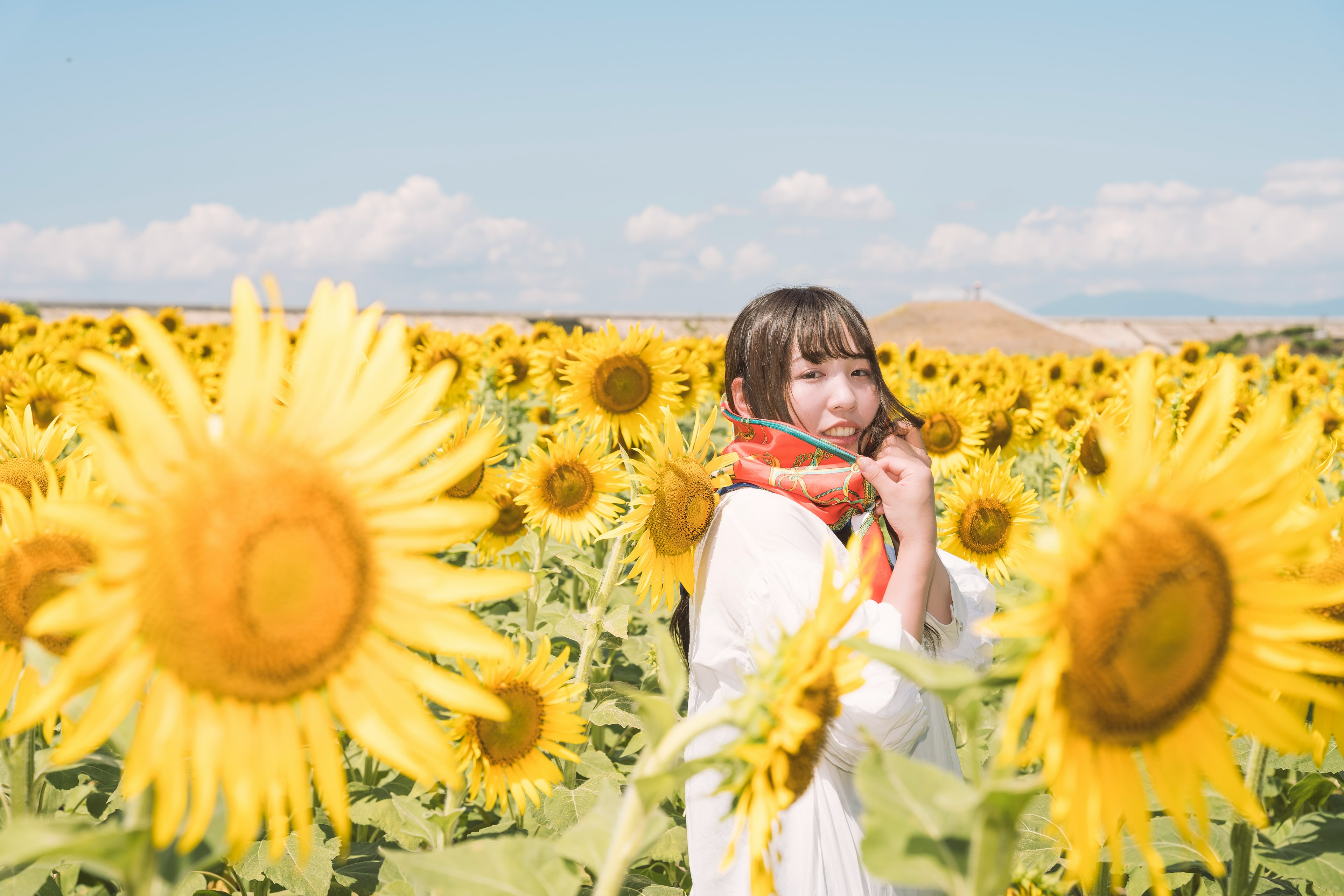 Woman smiling in a sunflower field wearing a white dress and orange scarf