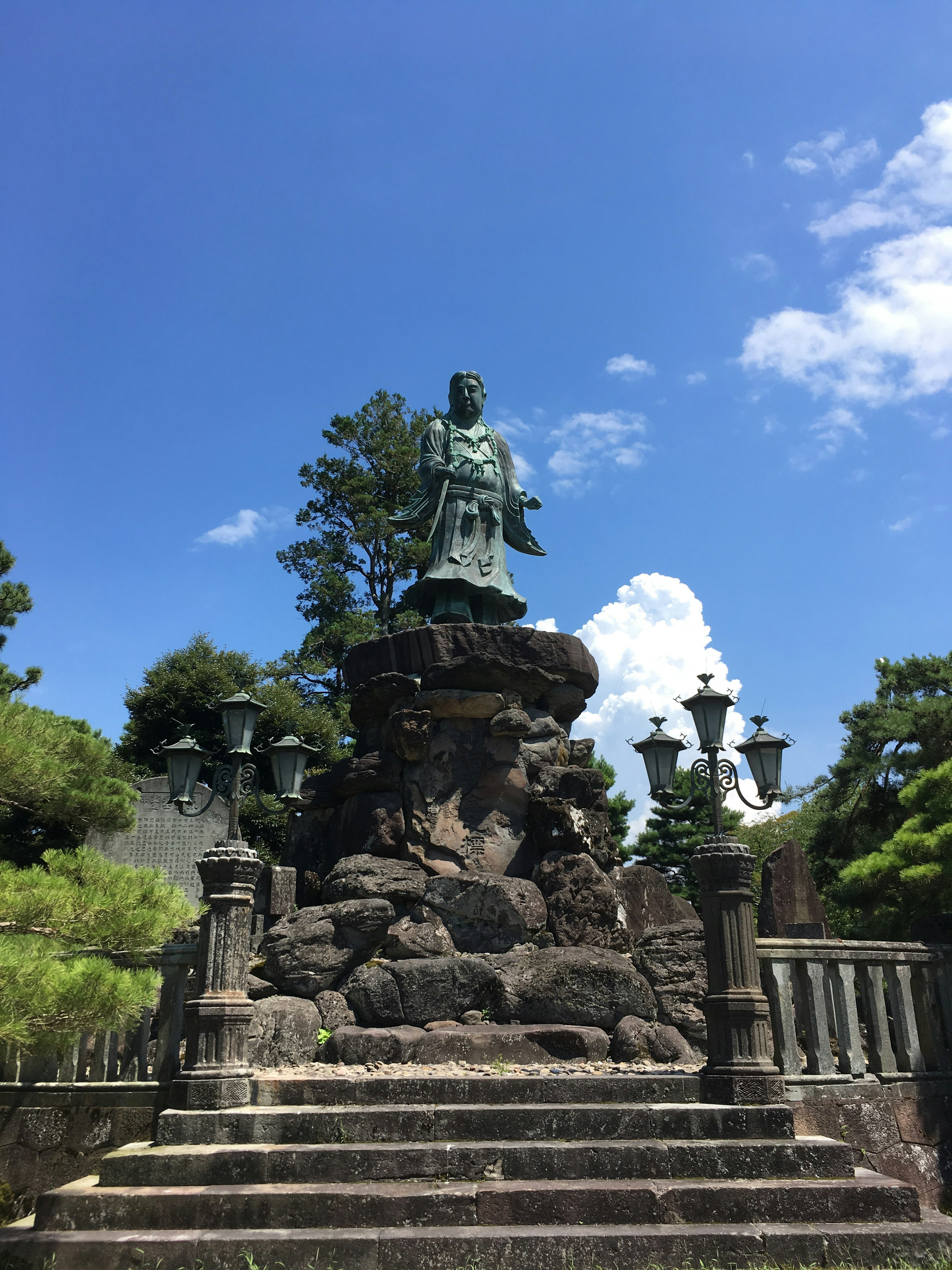 Estatua sobre un pedestal de piedra rodeada de árboles bajo un cielo azul