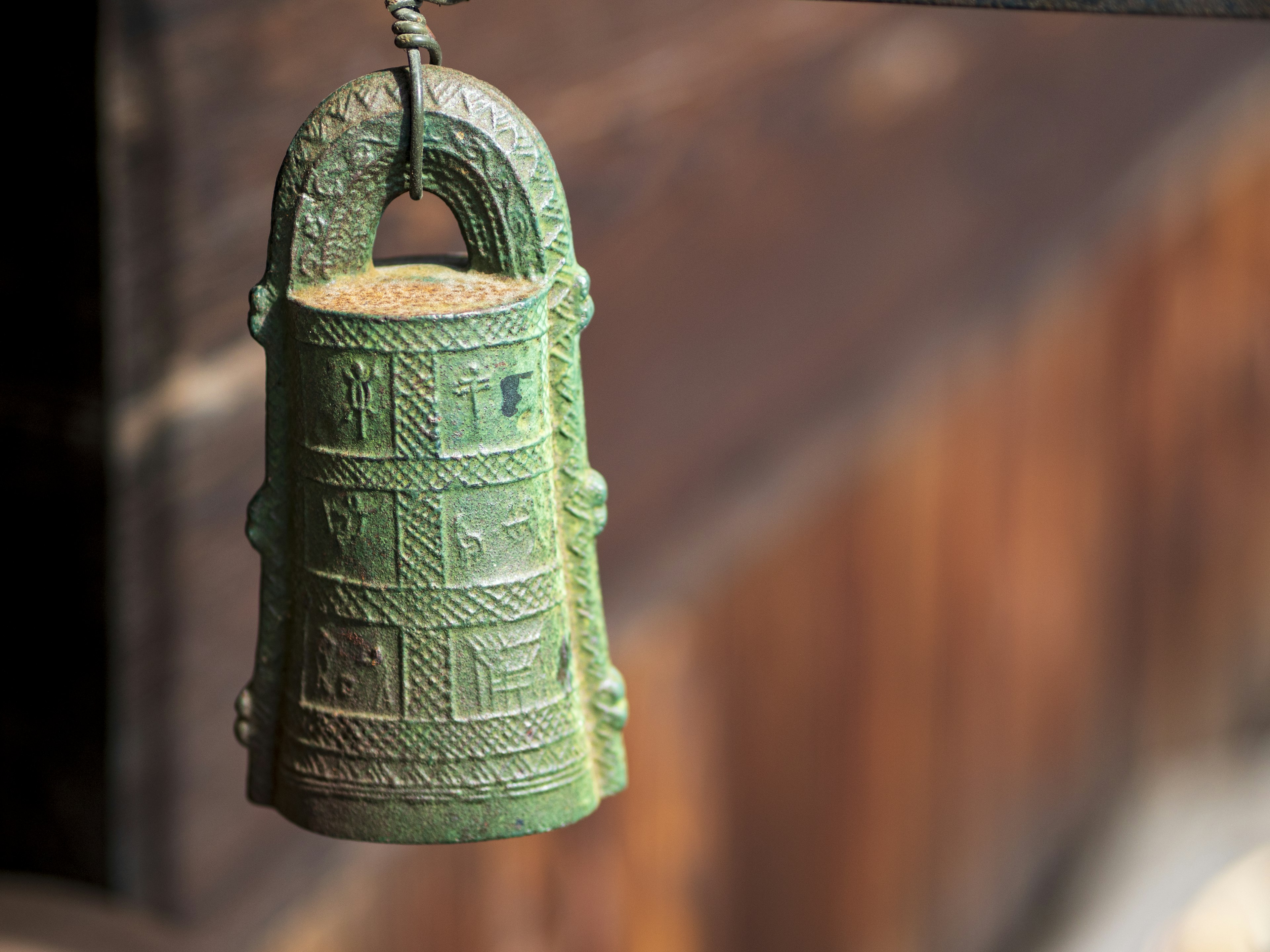 Eine alte Bronze-Glocke, die vor einem Holz-Hintergrund hängt