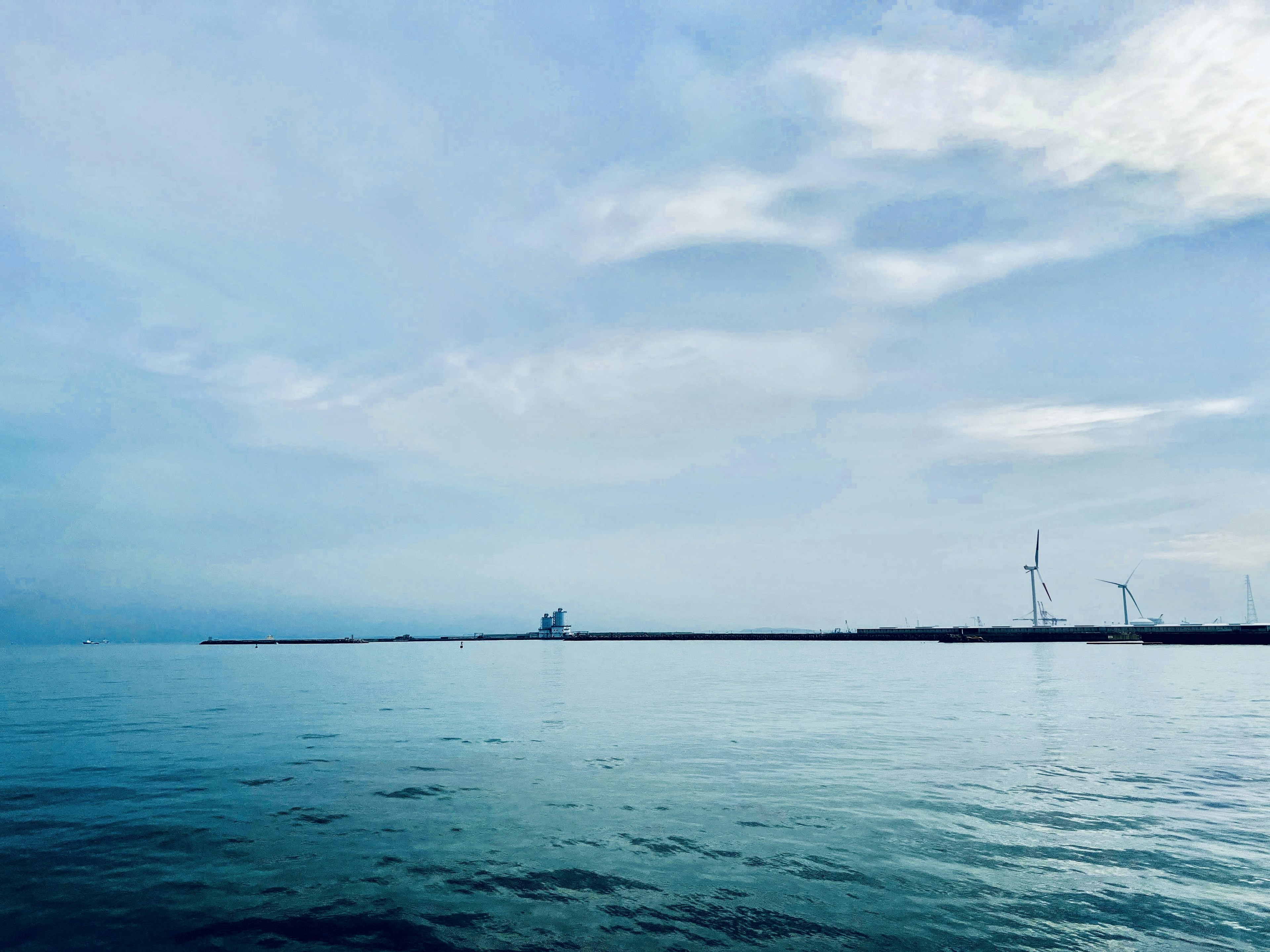 Calm sea with a blue sky and visible wind turbines