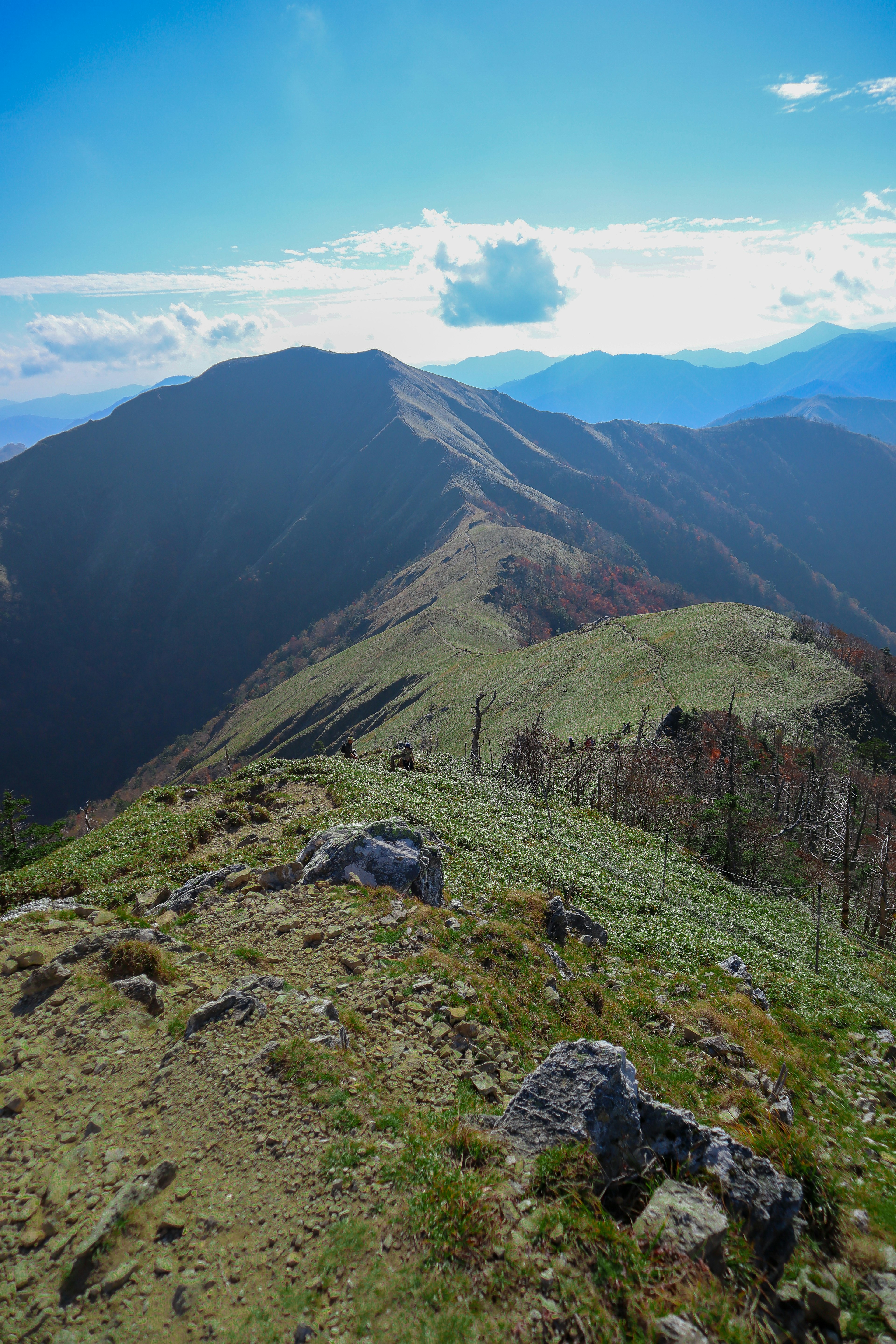 Vista de la cresta montañosa con cielo azul hierba verde y rocas dispersas