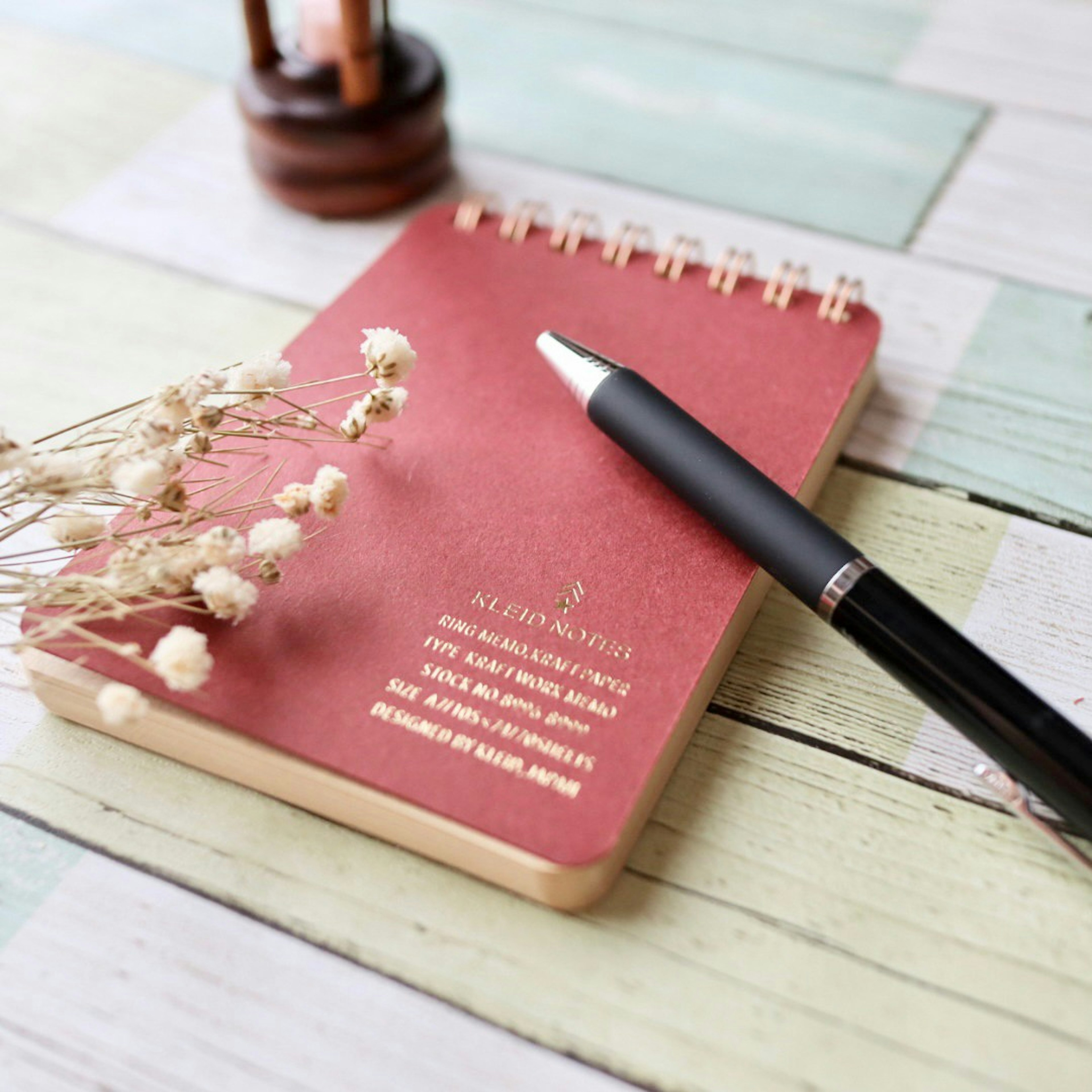 A red notebook and a black pen placed on a wooden table