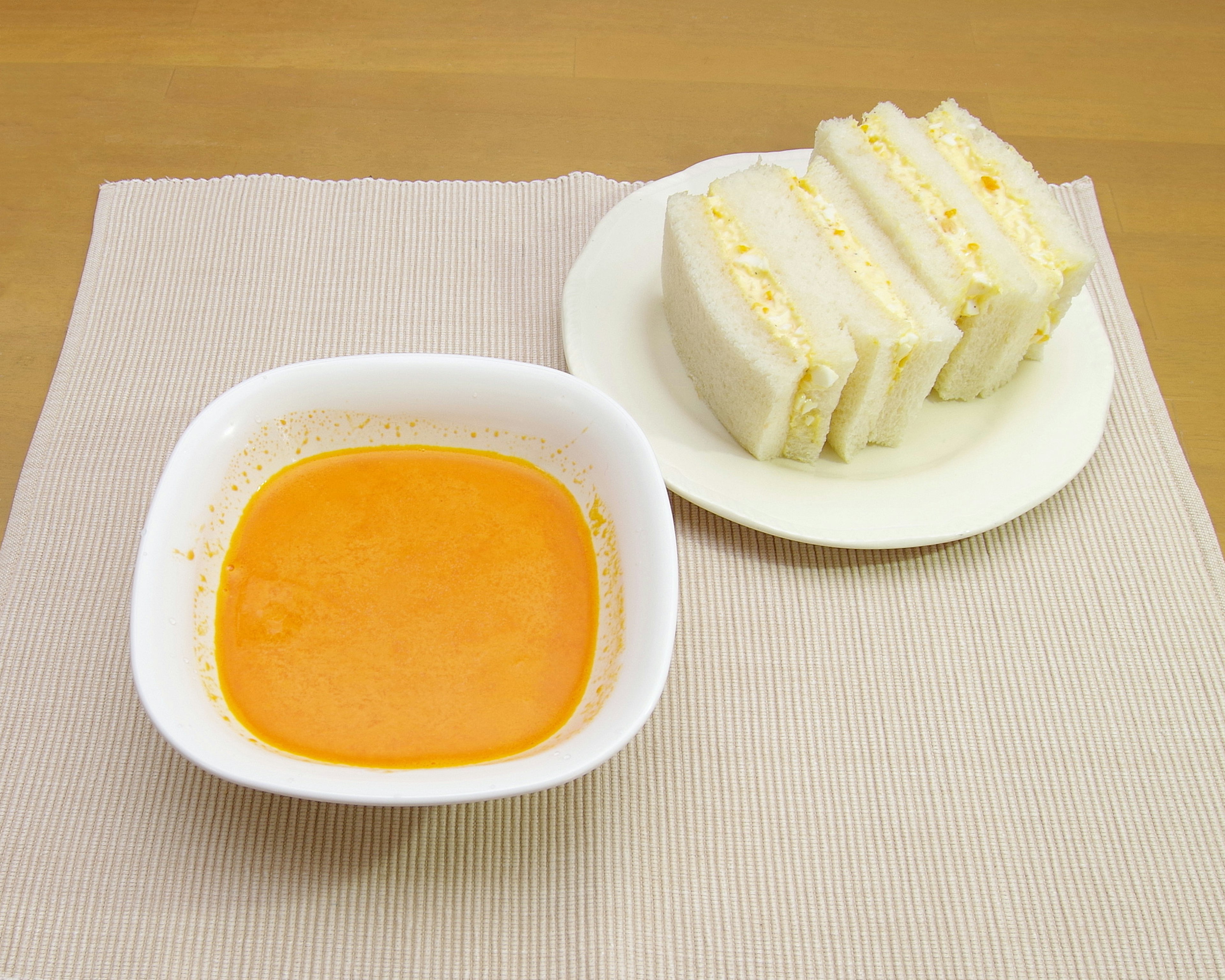 Ein Teller mit Sandwiches und eine Schüssel mit orangener Sauce auf einem beigen Platzdeckchen