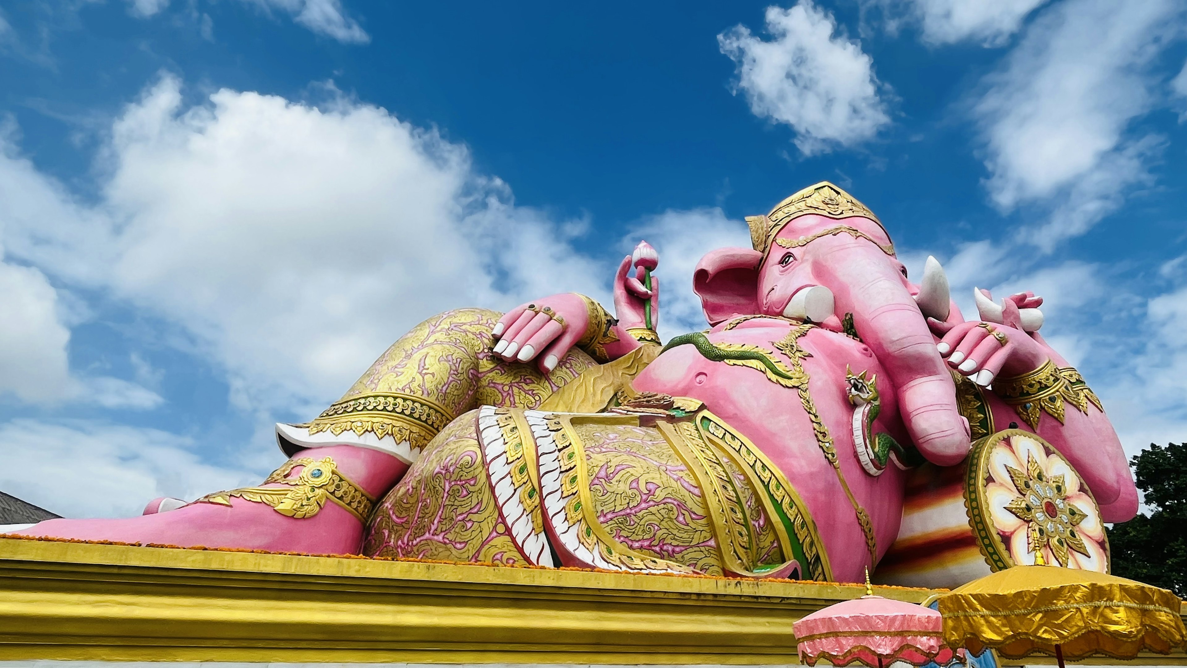 Patung besar berwarna pink dari Ganesha yang berbaring di bawah langit biru