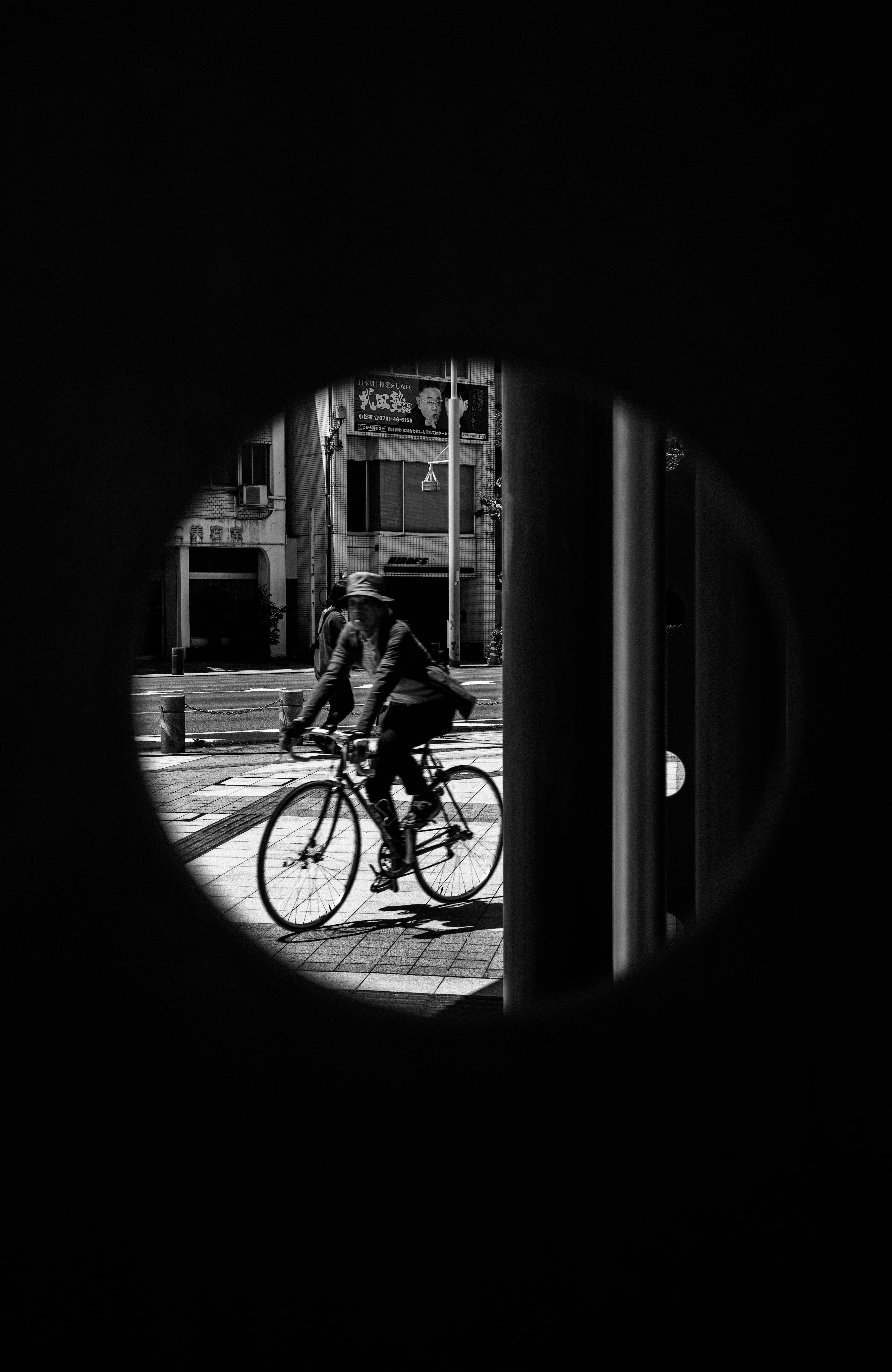 Una persona montando una bicicleta vista a través de una abertura circular en blanco y negro