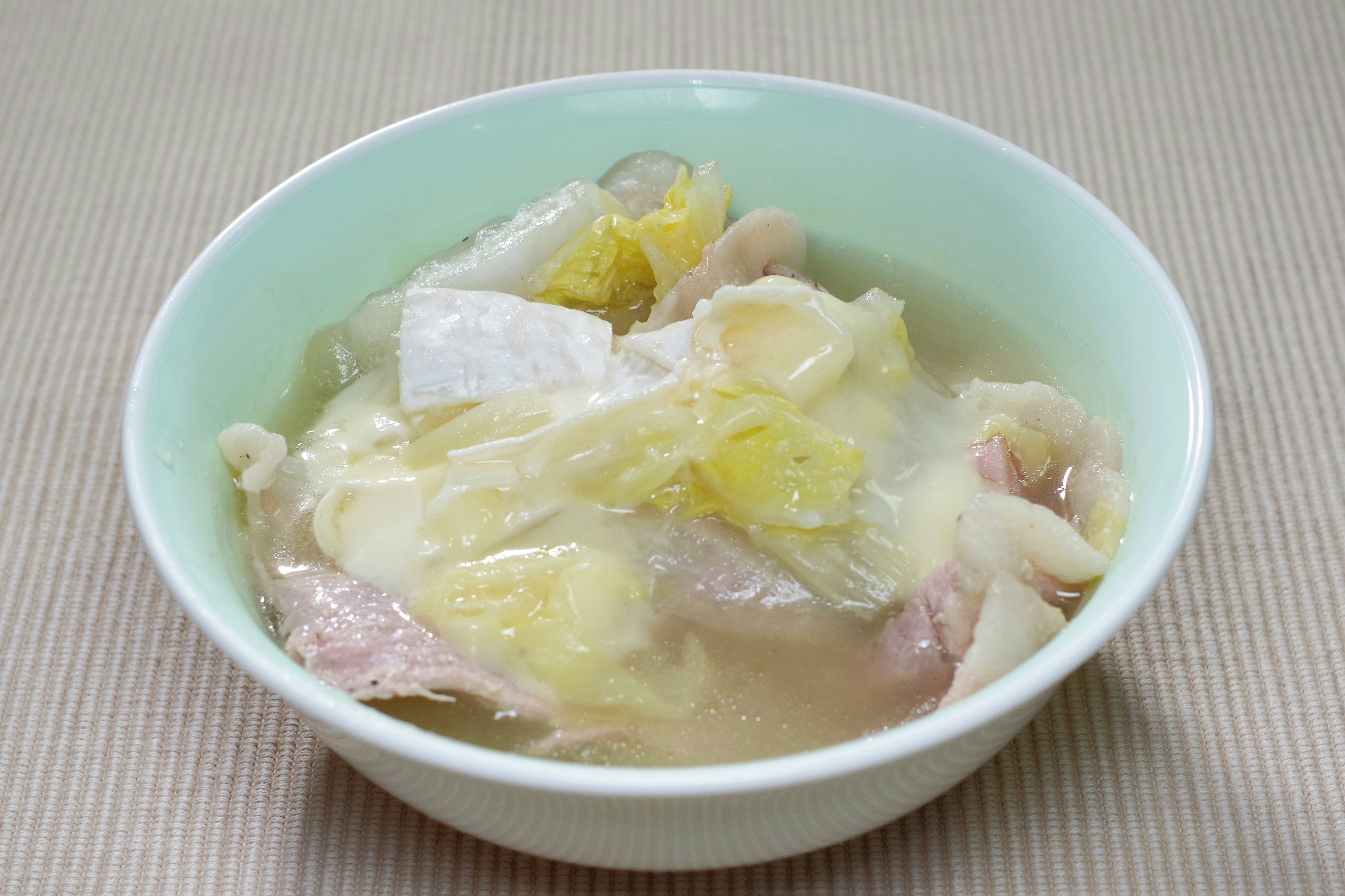 A shallow bowl containing chicken and napa cabbage soup