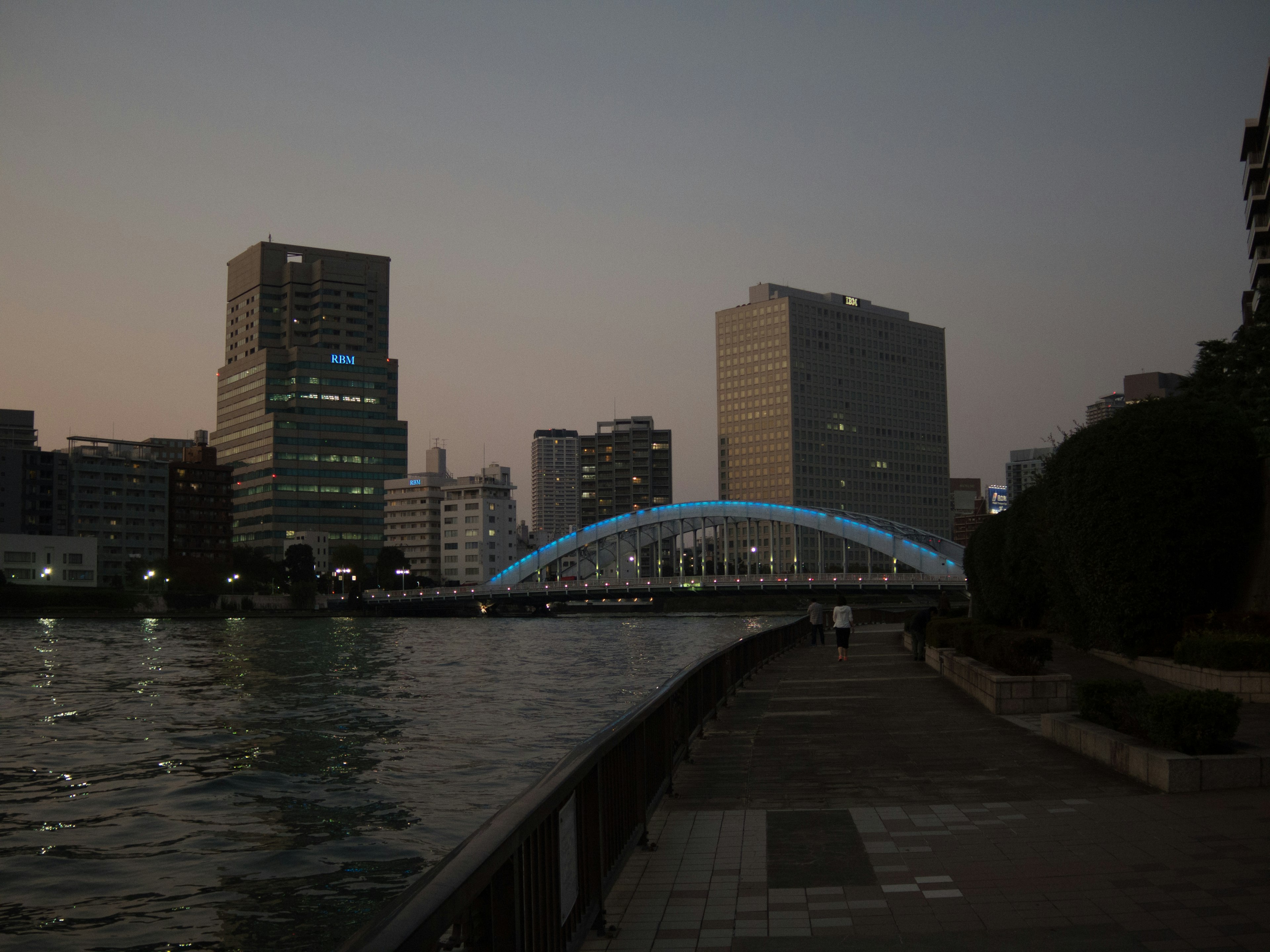 夕暮れ時の都市景観に映える青い光を放つ橋と高層ビル群