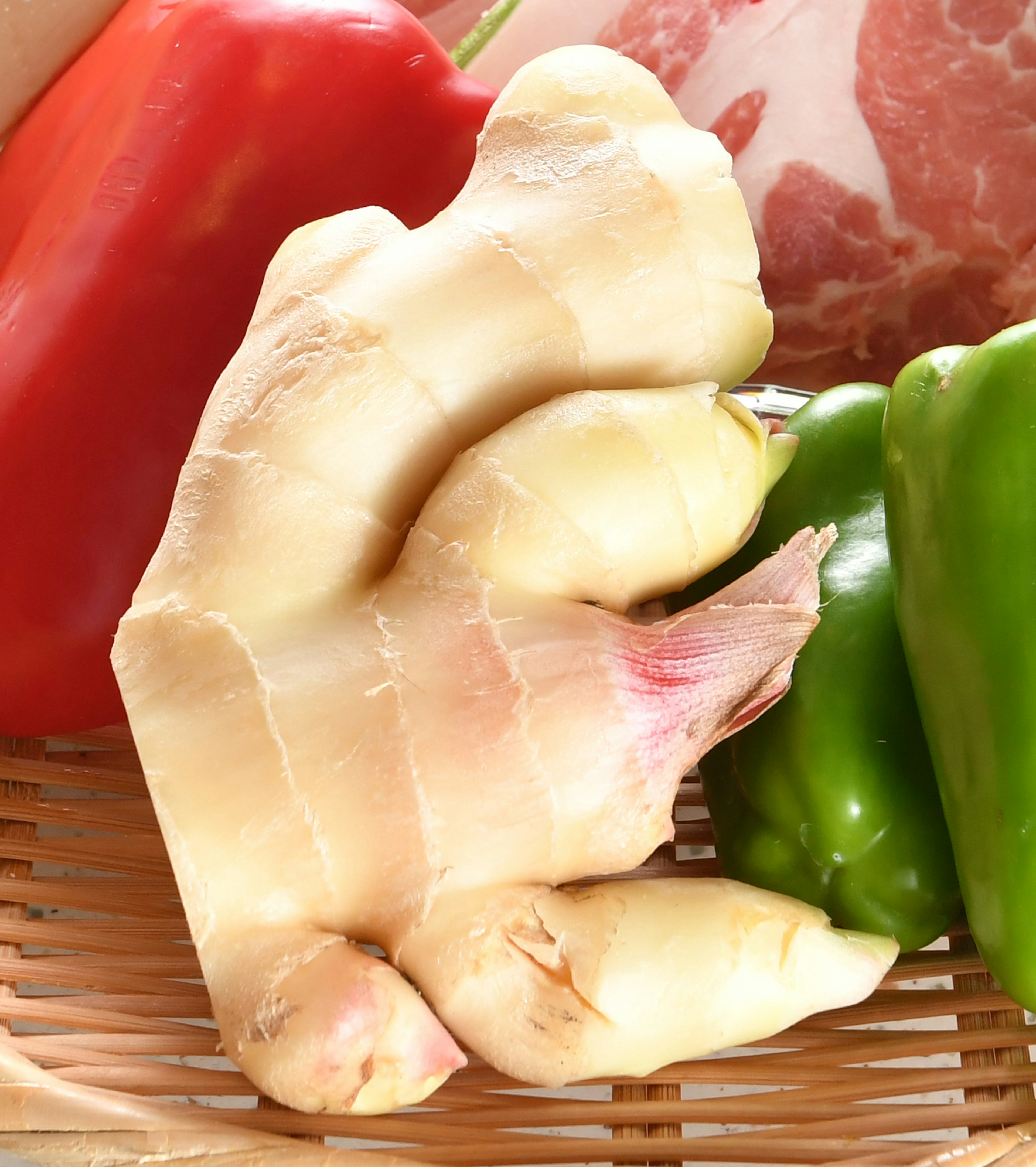 Fresh ginger root surrounded by vibrant red and green vegetables