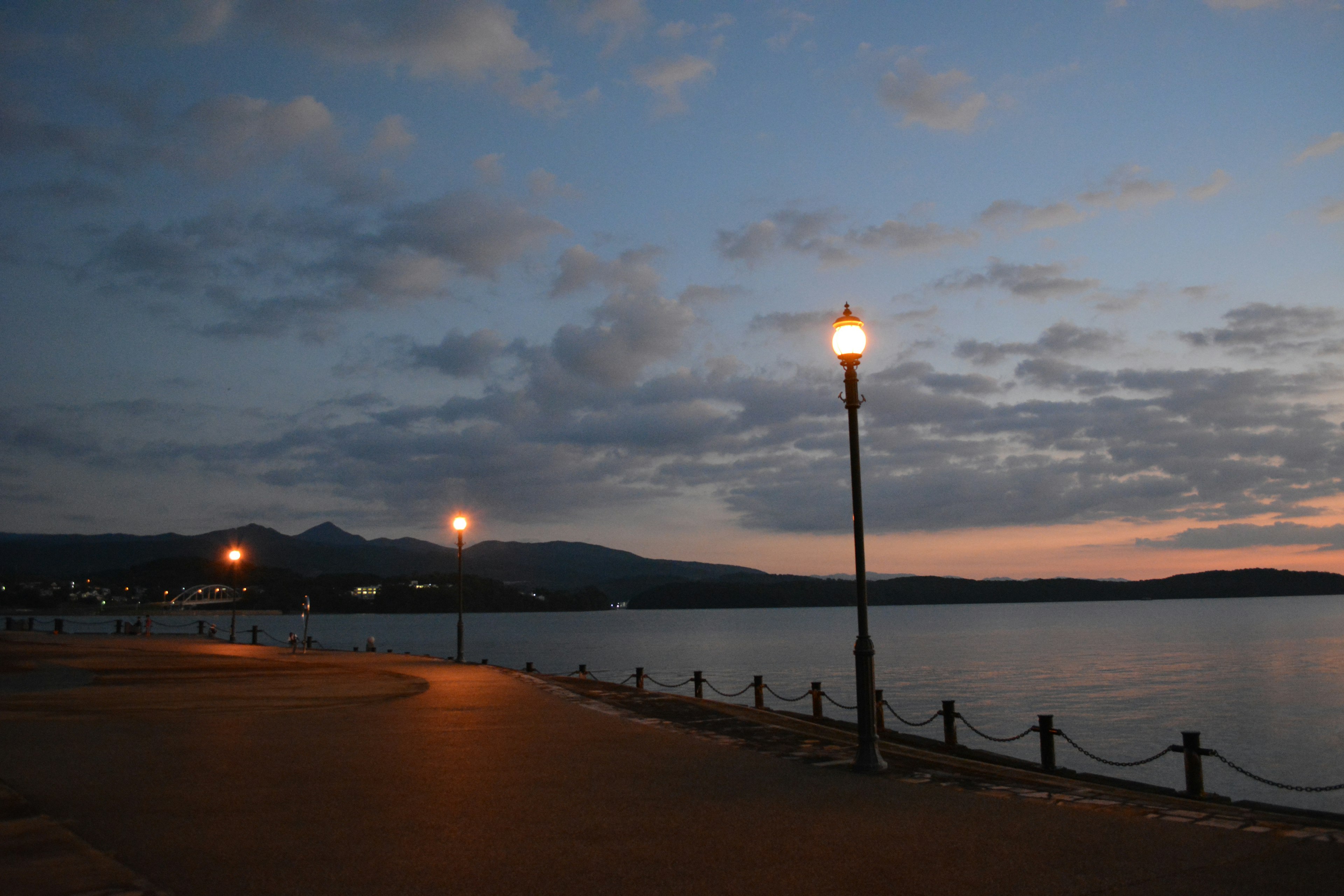 Twilight lakeside scene featuring a lamp post along a walkway and calm water