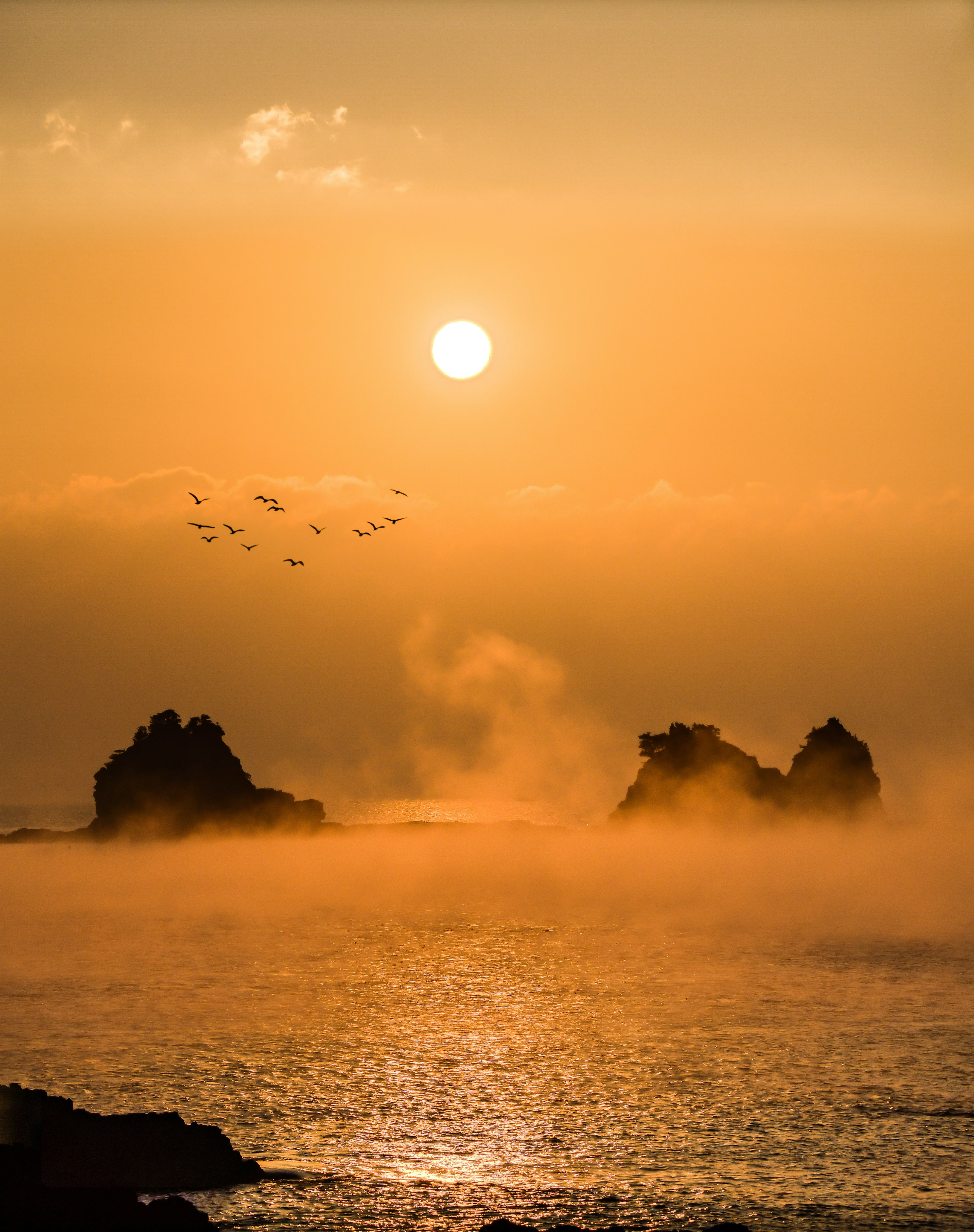 オレンジ色の夕日が海に沈むシーン 岩と霧が幻想的な雰囲気を演出