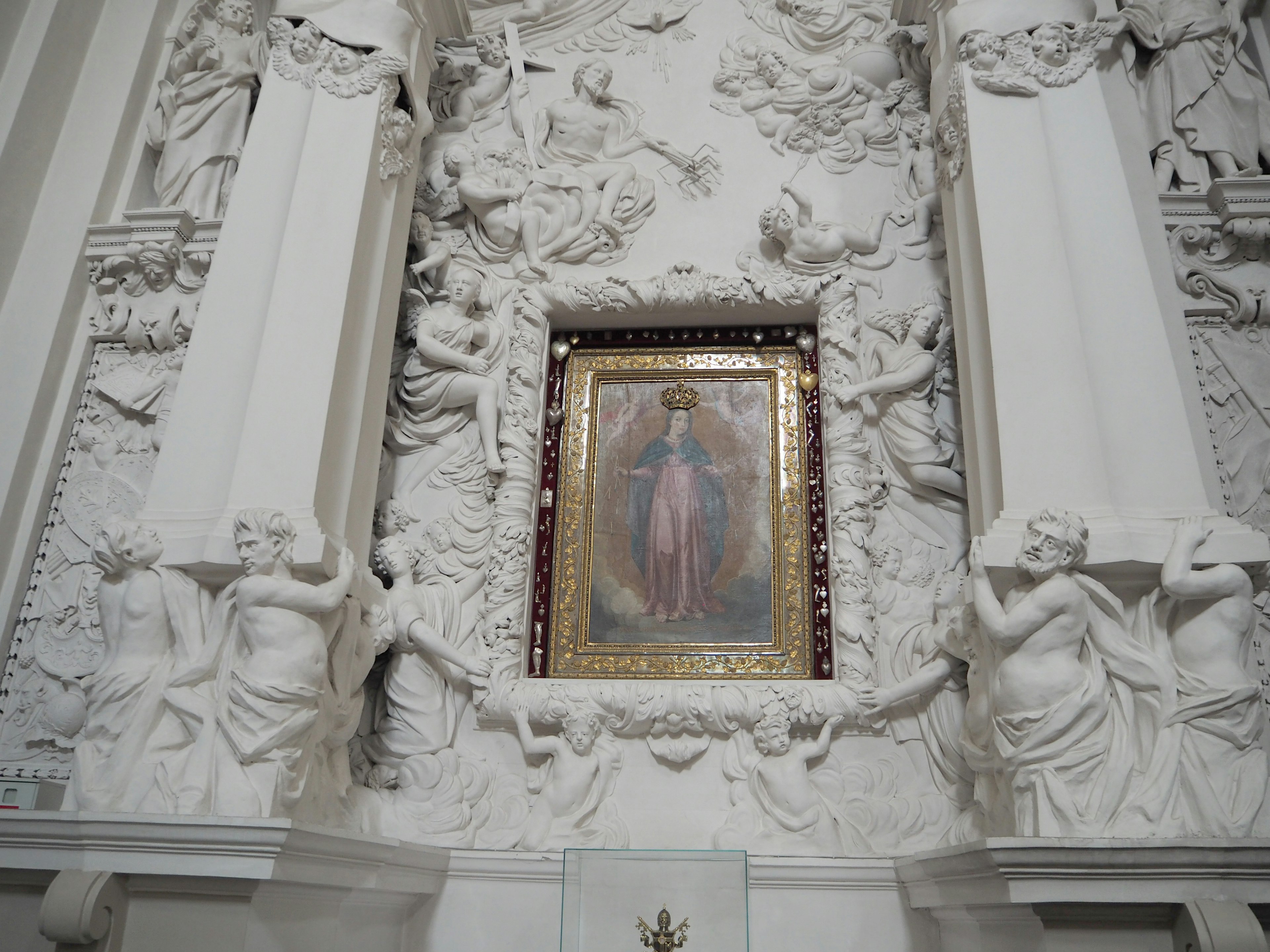 Religious painting framed by ornate white sculptures on the wall