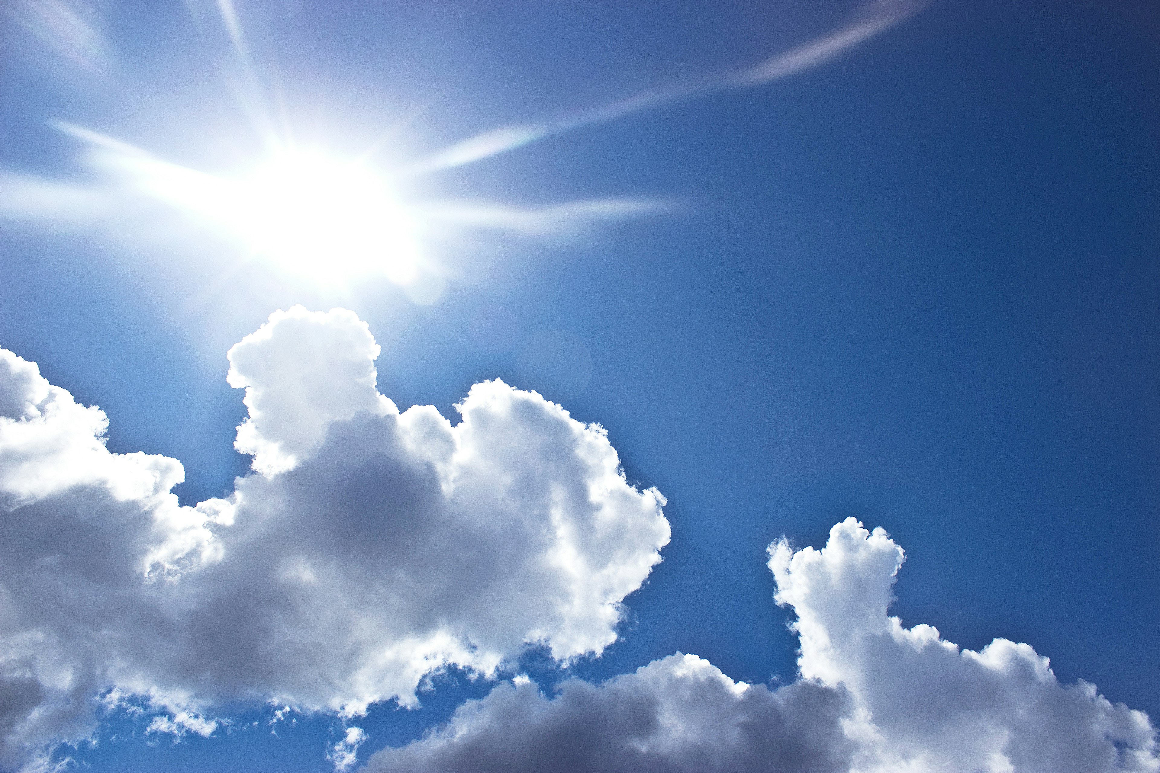 青空に浮かぶ白い雲と眩しい太陽