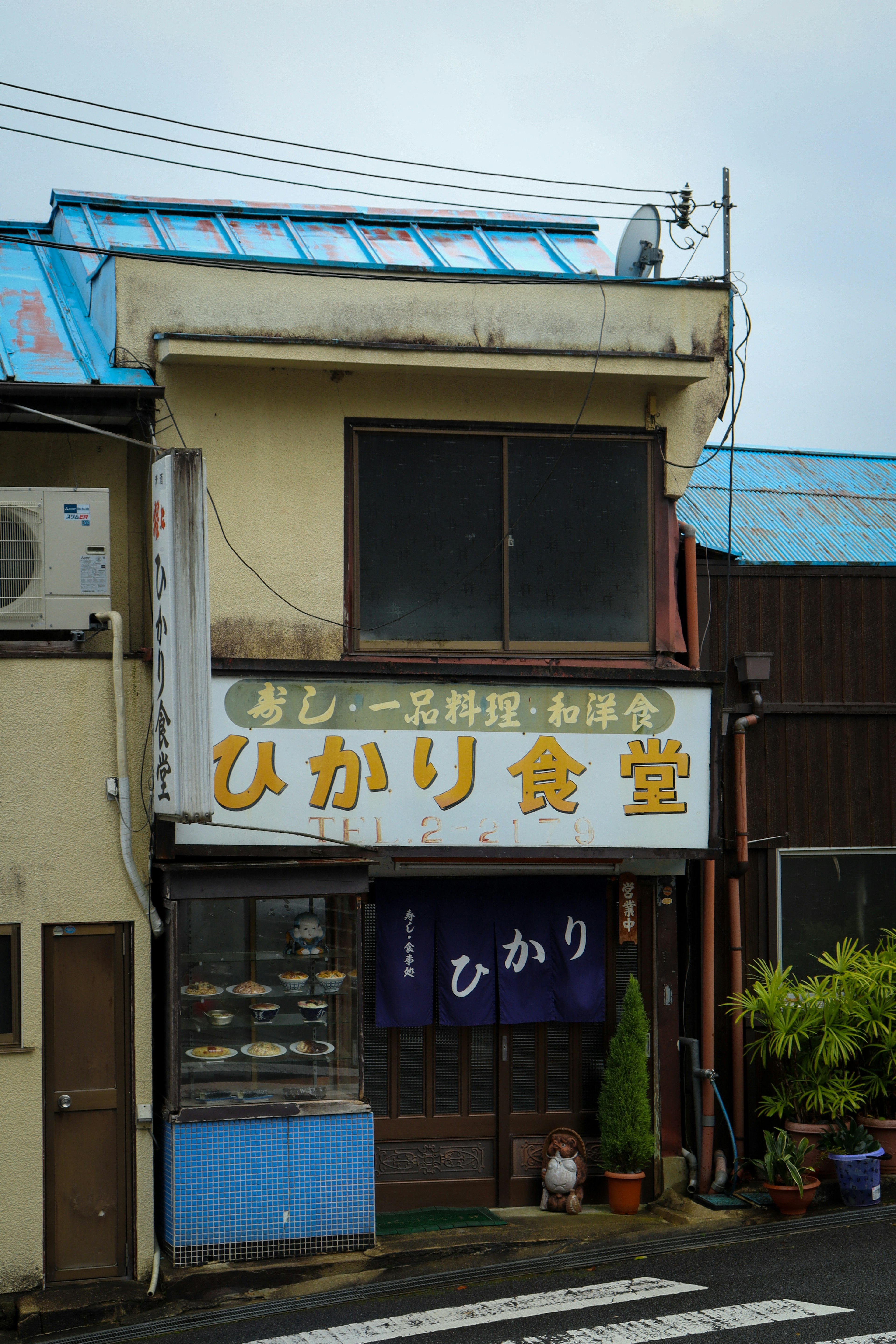 光食堂外观 蓝色屋顶和白色招牌 植物和人行横道可见