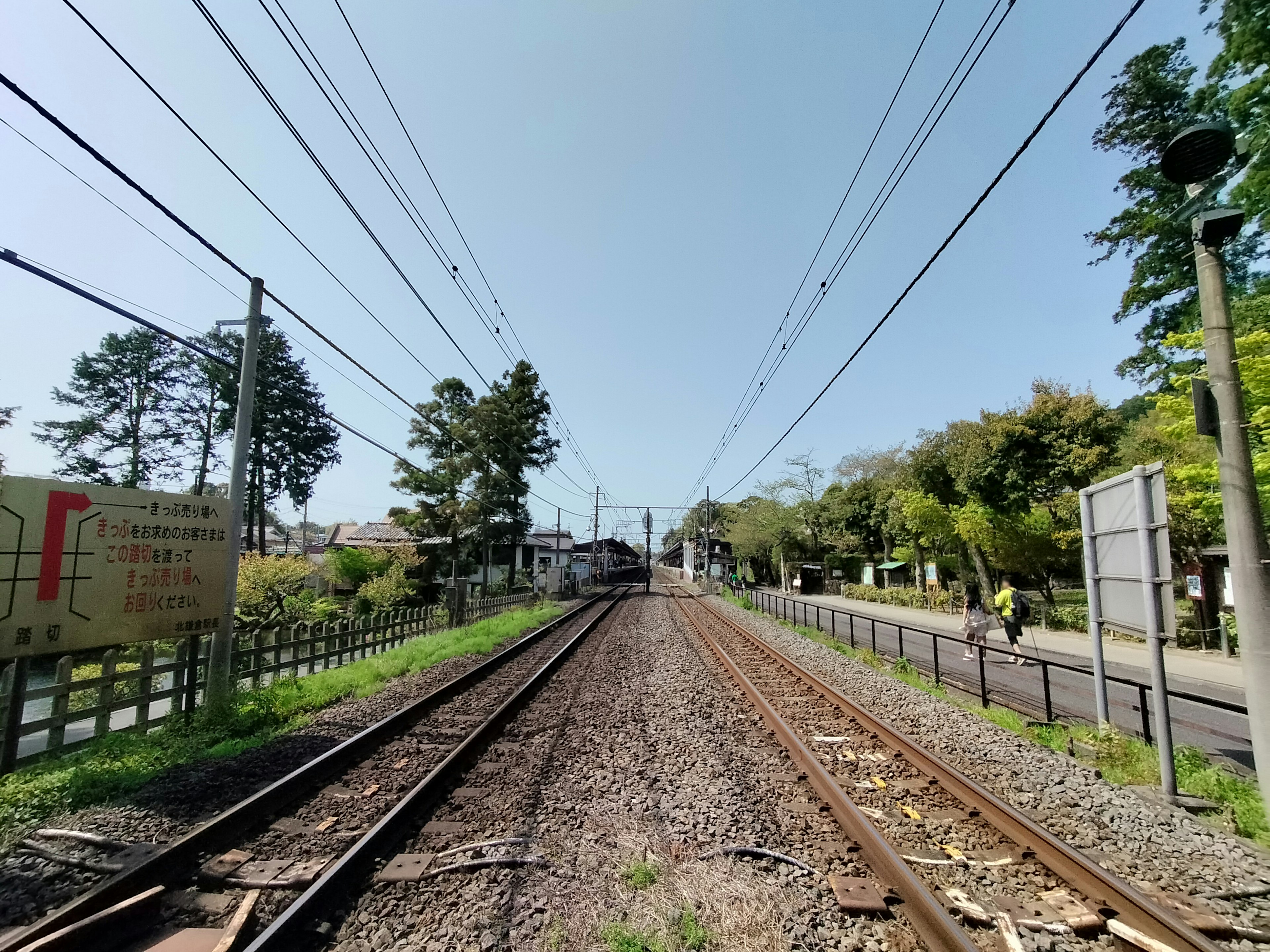 Vue des voies ferrées menant à une gare avec ciel bleu clair et arbres verts