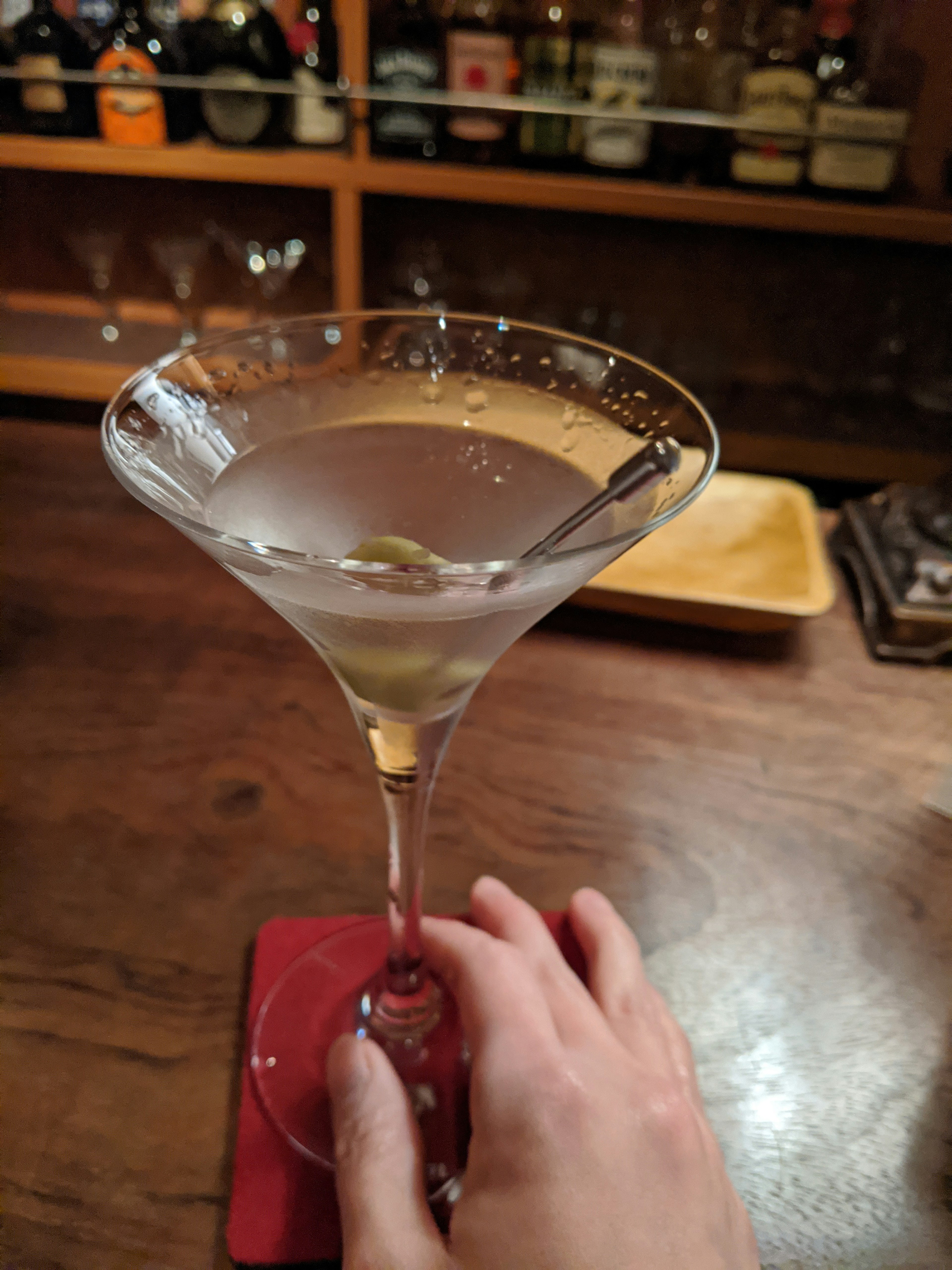 A hand holding a martini glass with an olive cocktail