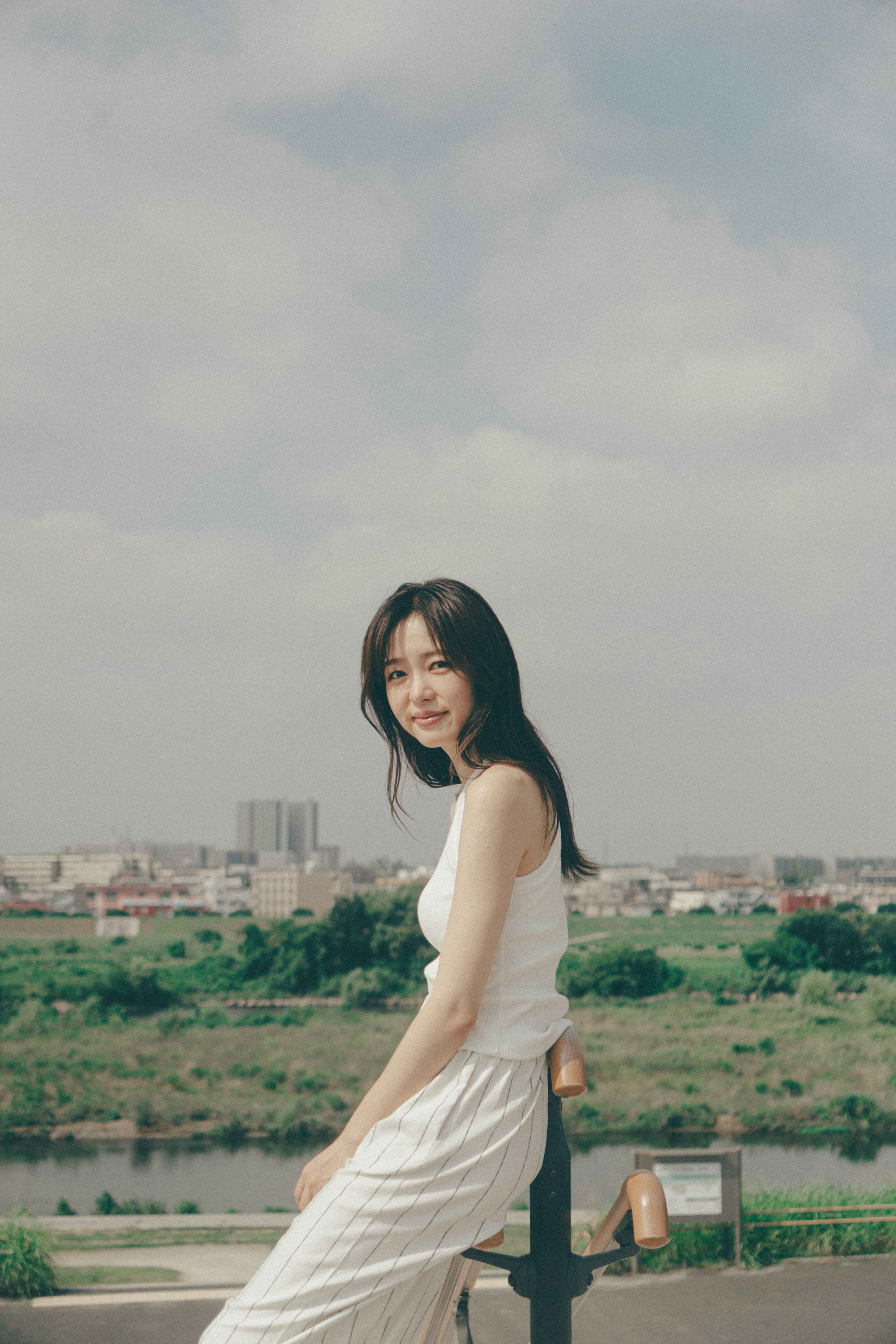 Portrait of a woman sitting by the riverside with a clear sky and green landscape