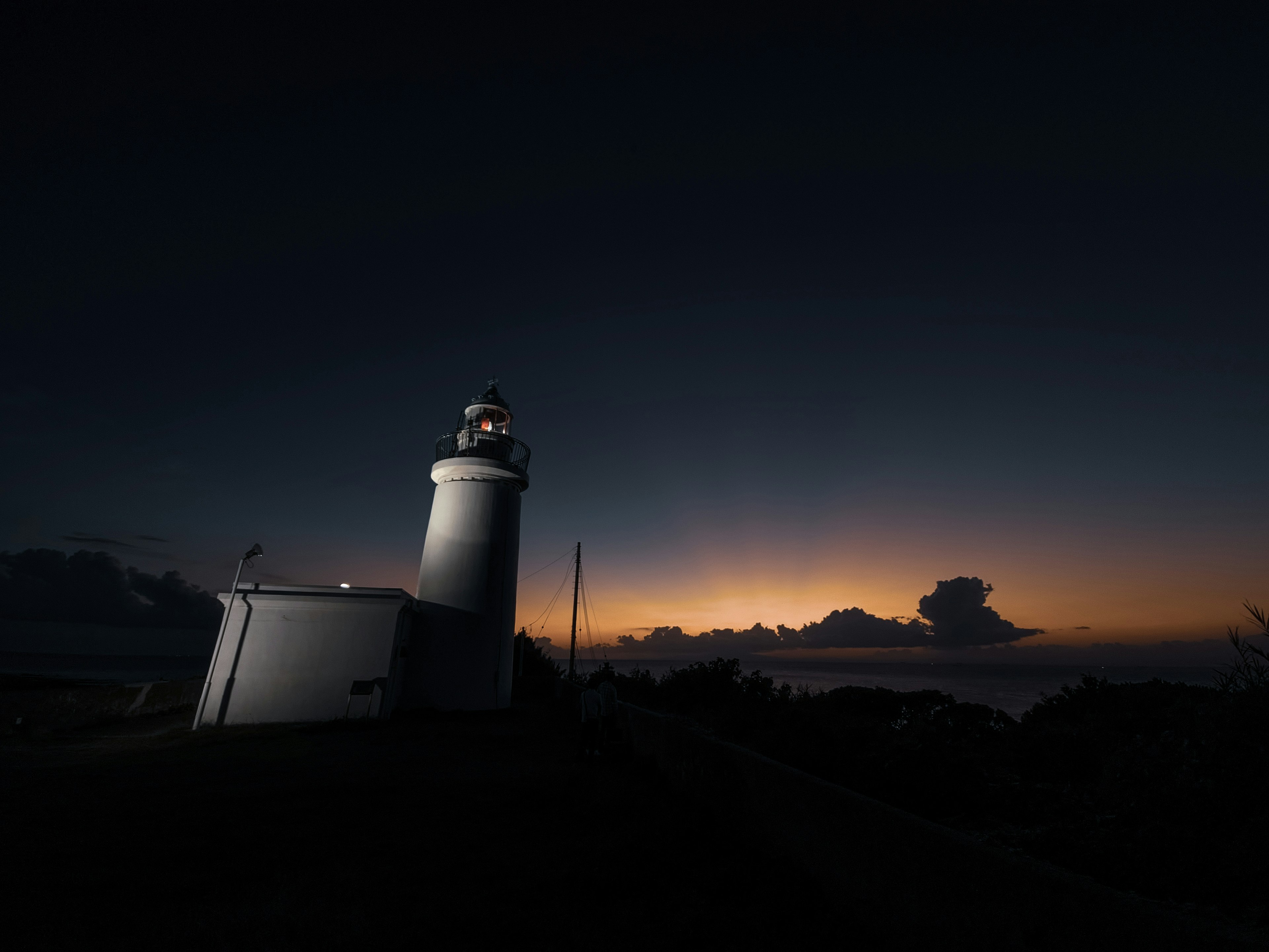 Lighthouse silhouetted against a dark sky at dawn