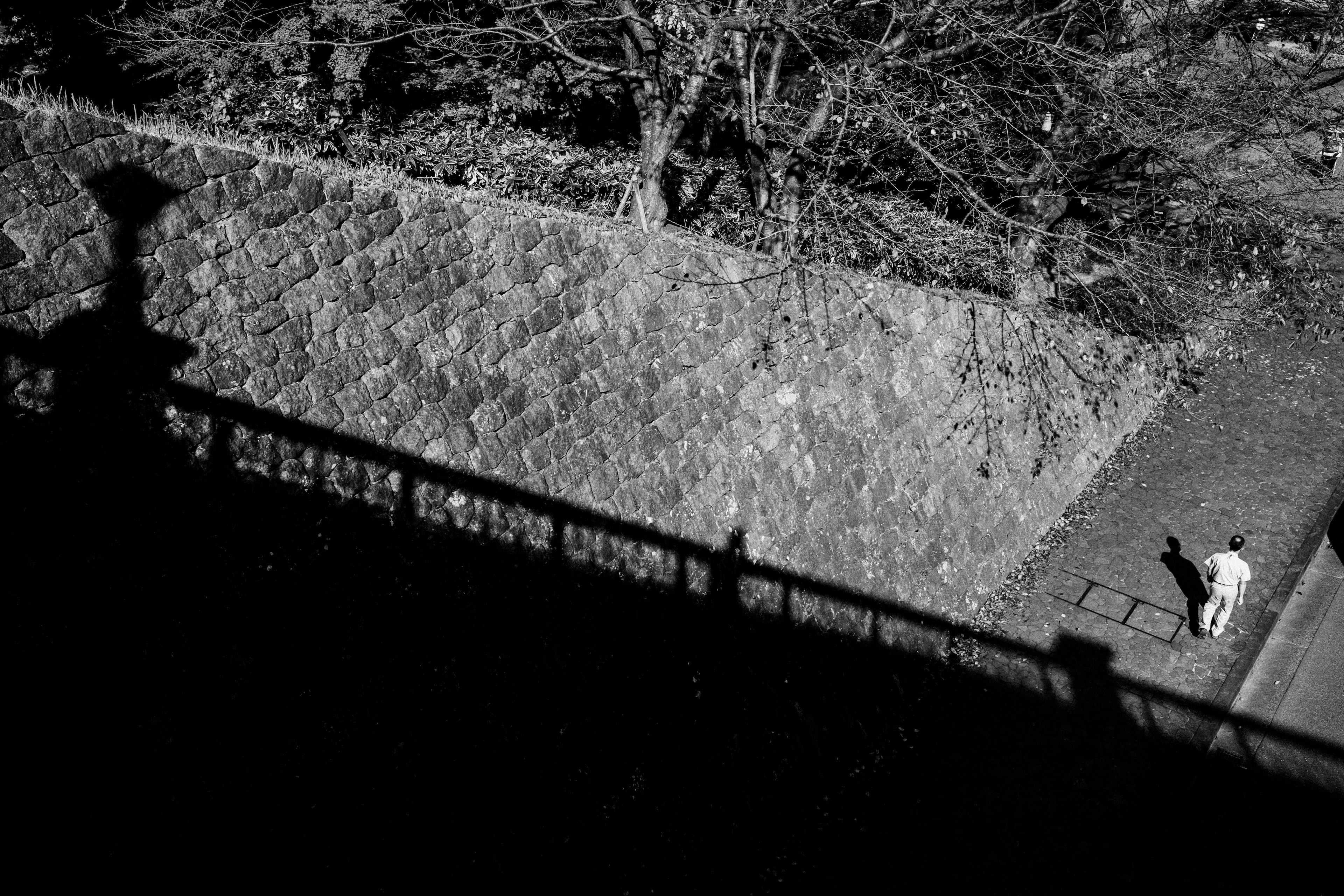 Person walking along a stone wall with shadows