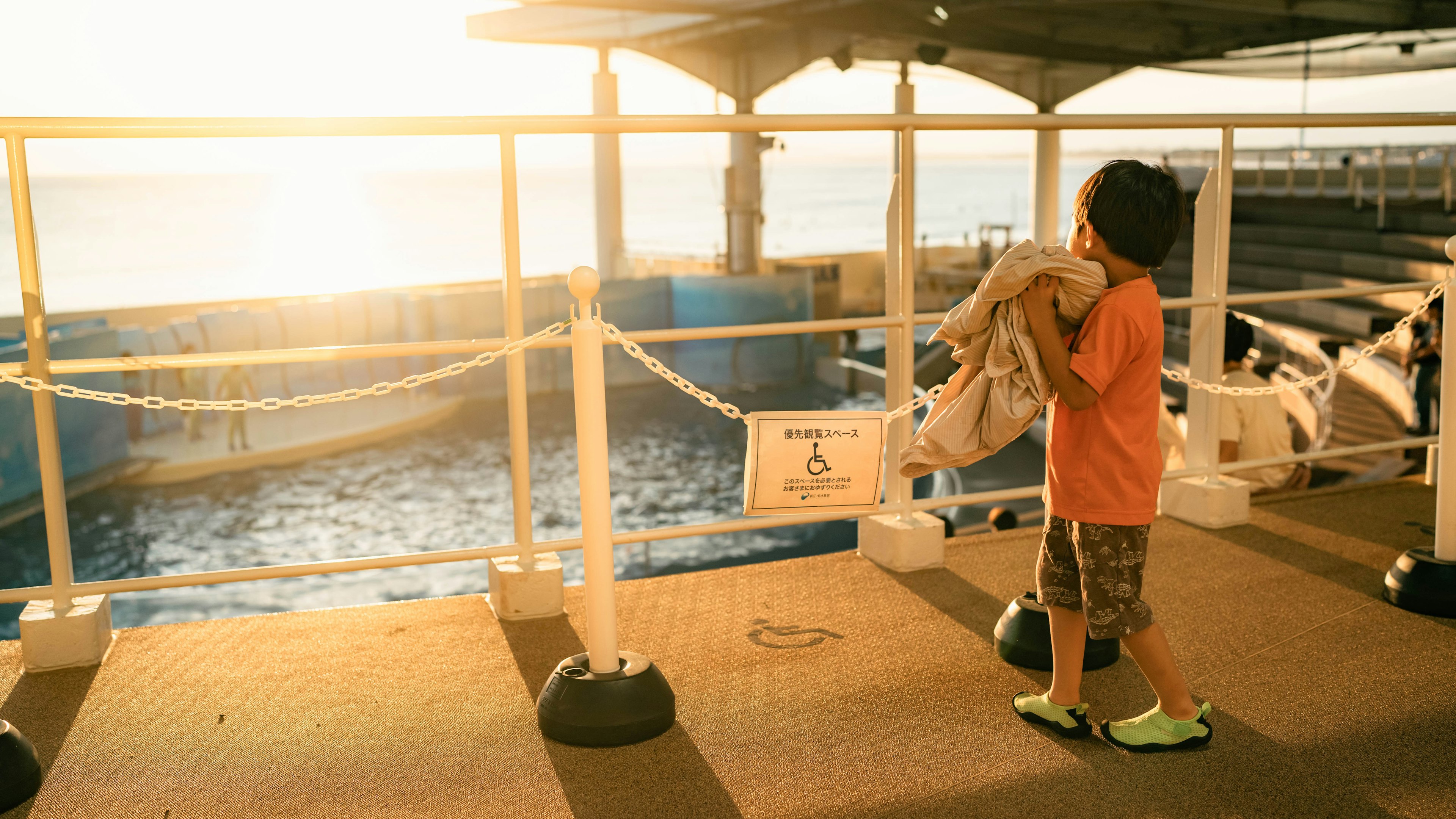 Boy standing by the sea holding a bag sunlight reflecting on water evening harbor scene