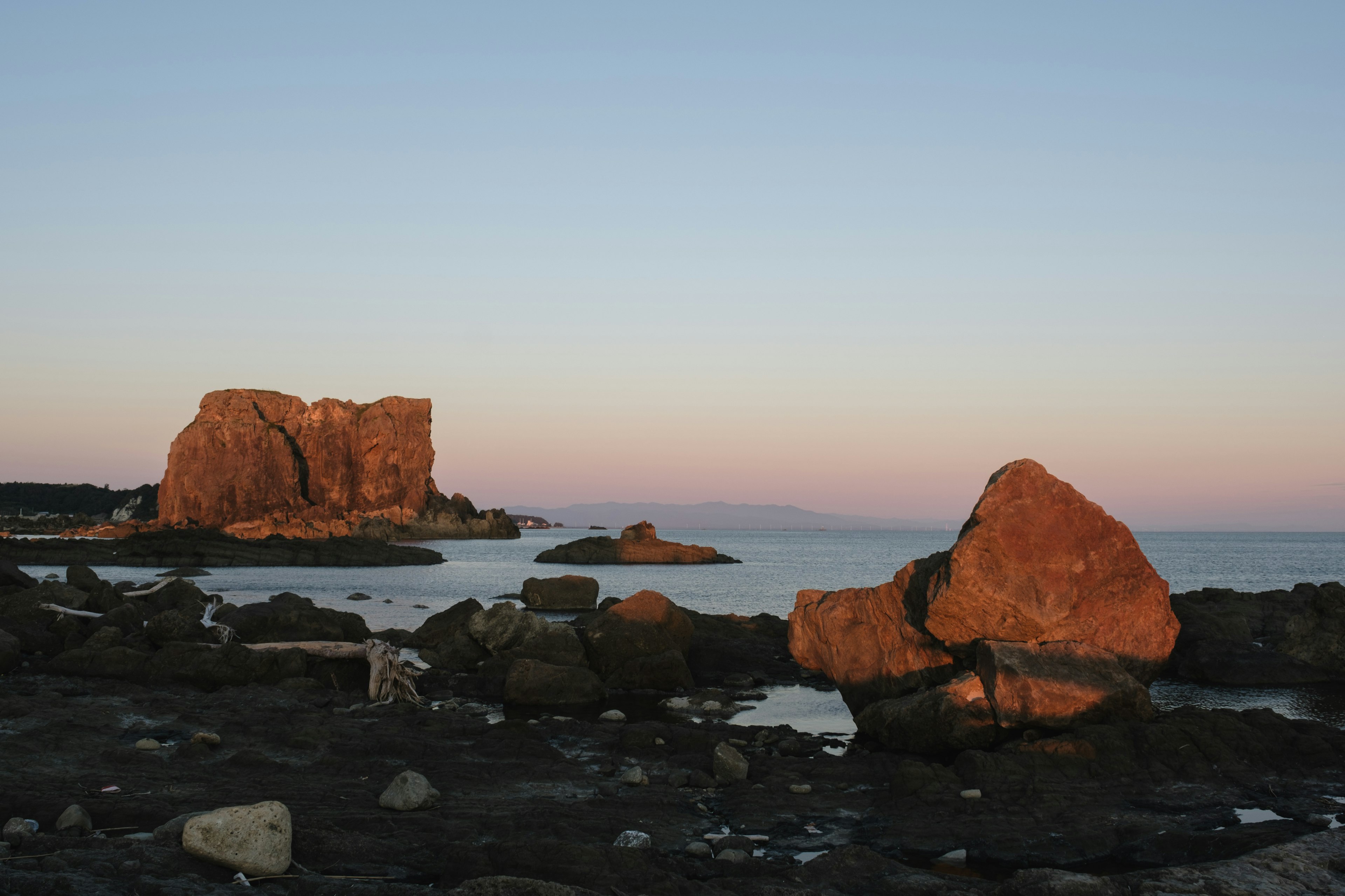 夕日を背景にした海岸の岩と穏やかな海