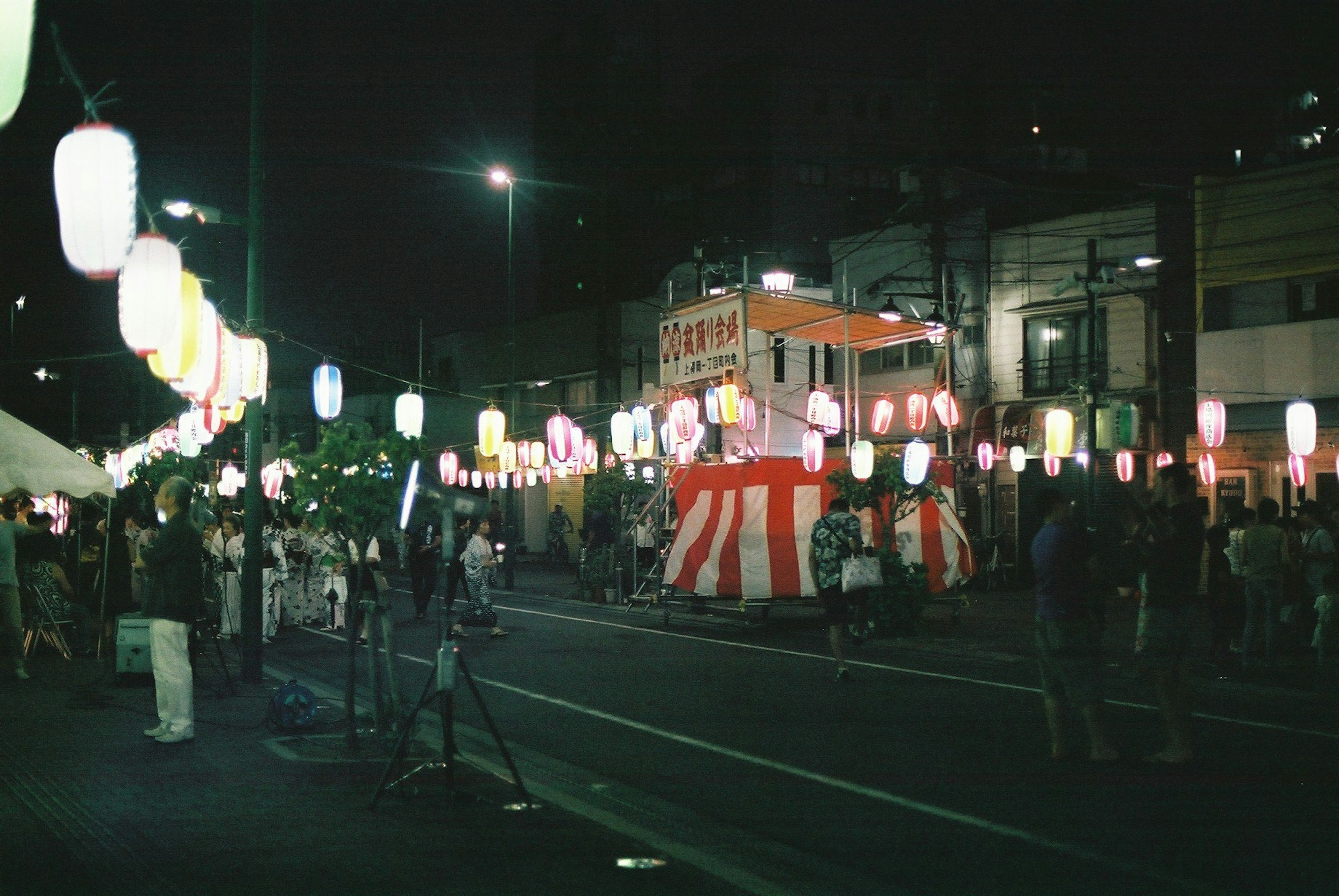 Multitud en un festival nocturno con faroles iluminados y un puesto de comida