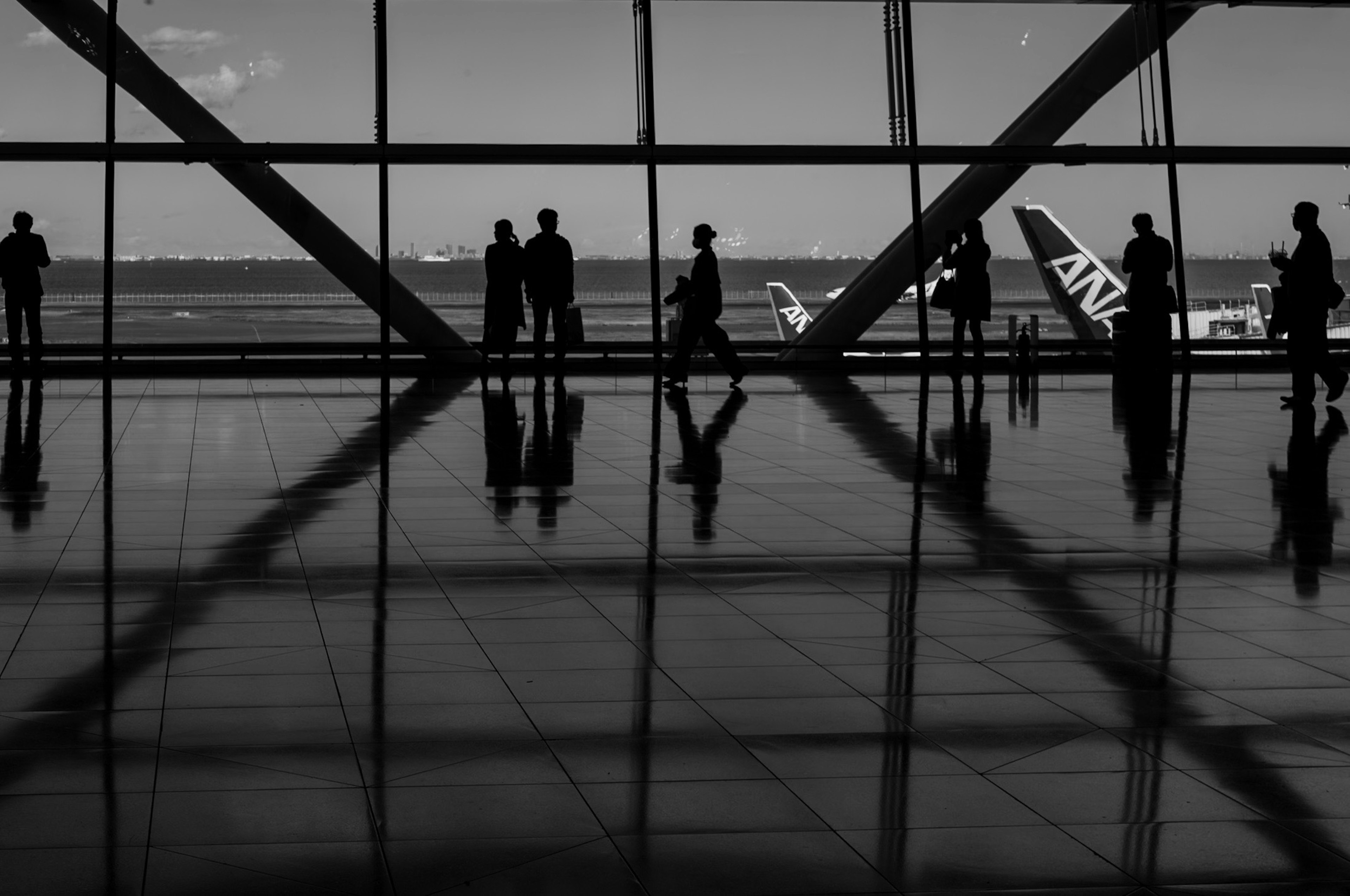 Siluet orang-orang di terminal bandara dengan pesawat ANA di latar belakang